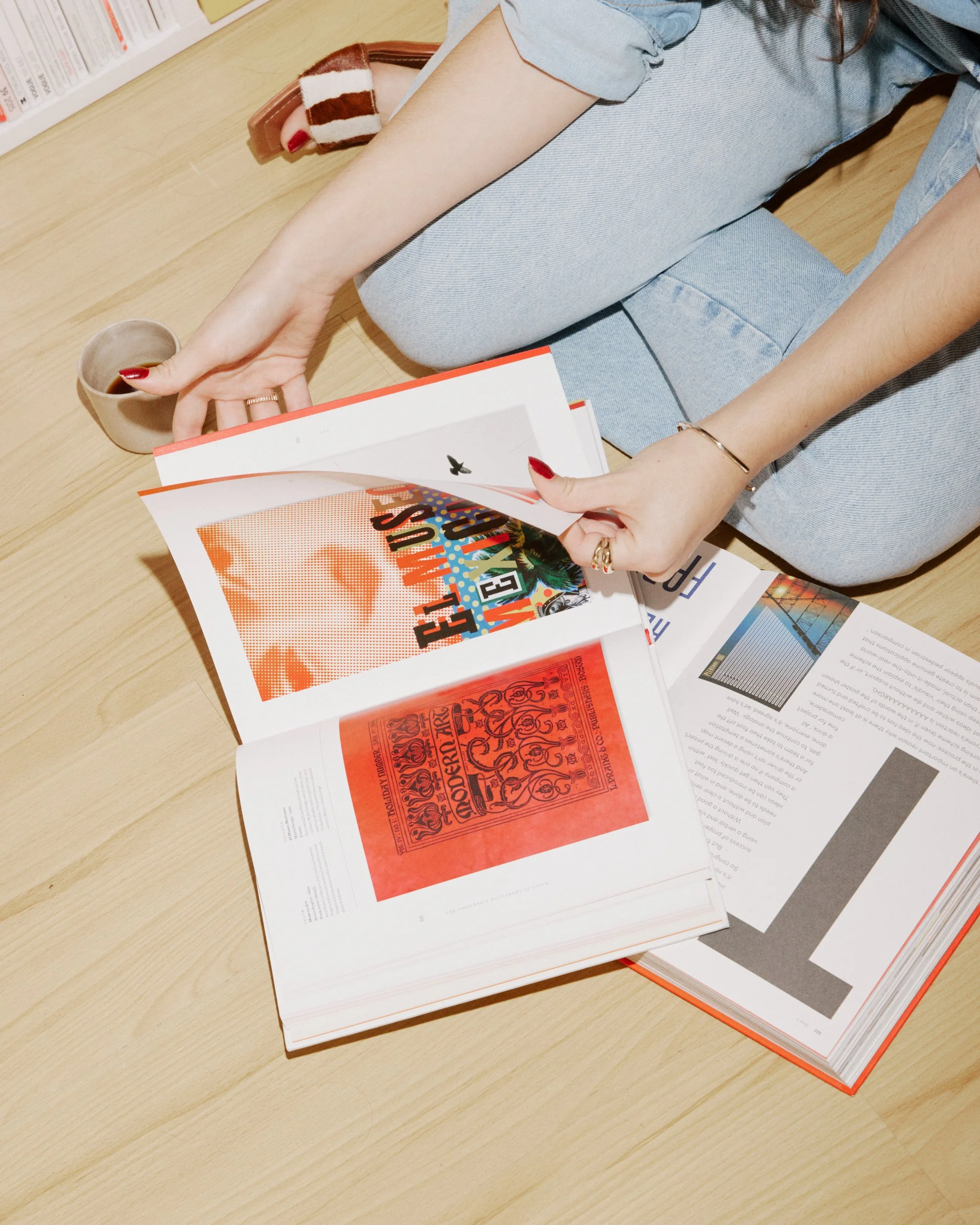 Pessoa sentada no chão folheando revistas em uma mesa de madeira, com uma xícara ao lado.