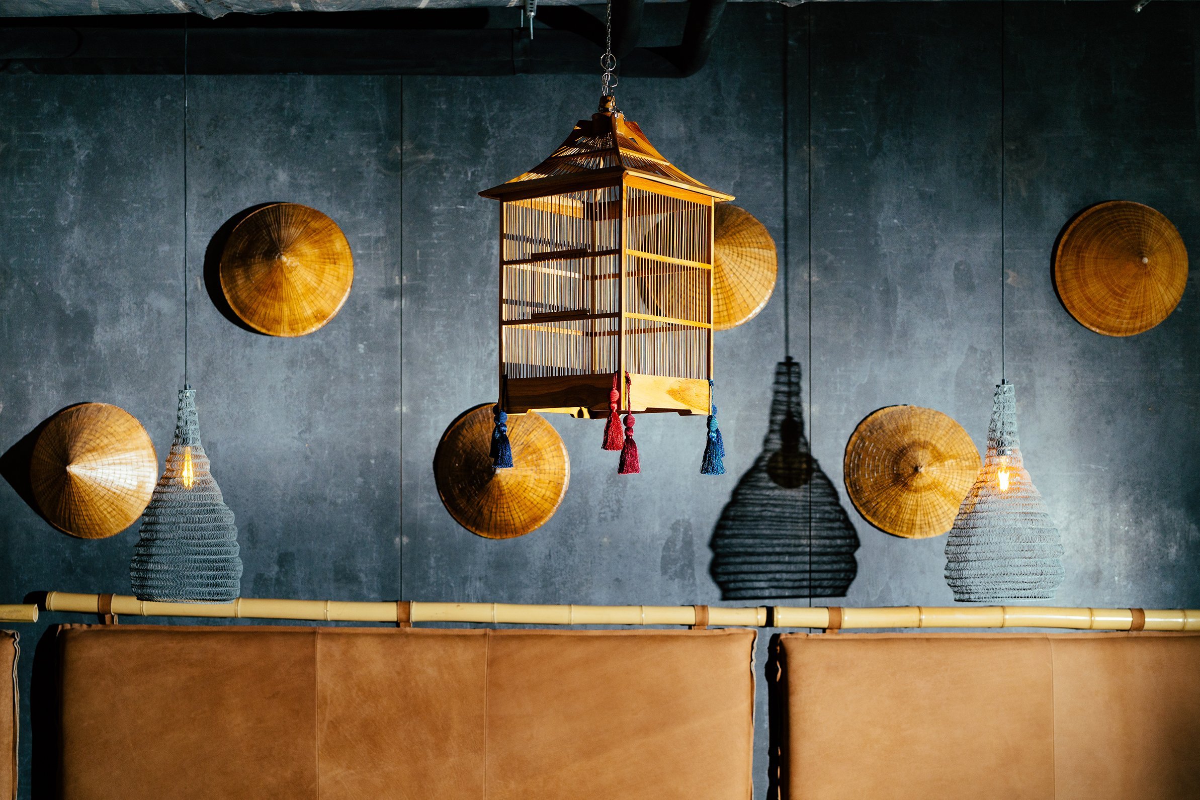 Decorative hanging lantern, woven pendant lights, and bamboo wall decor on a dark textured wall in a restaurant or cafe interior.