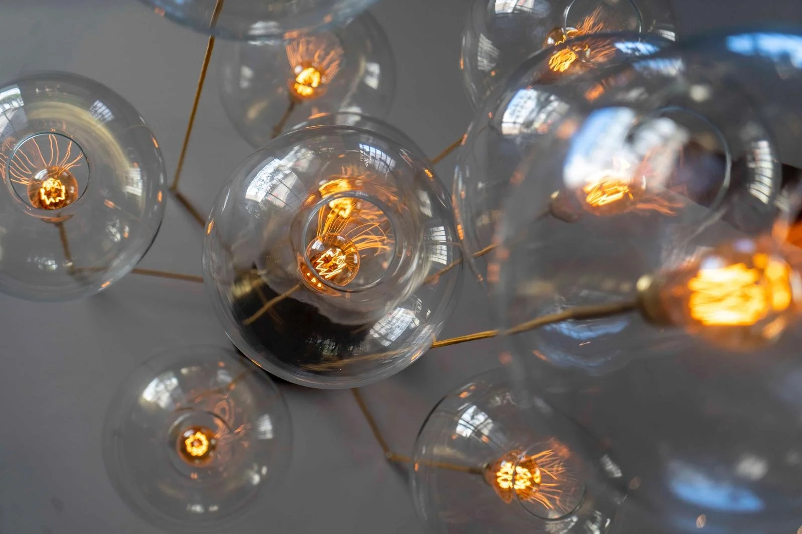 A modern chandelier with multiple clear glass globe light bulbs, some lit with warm orange filaments, hanging at different heights.