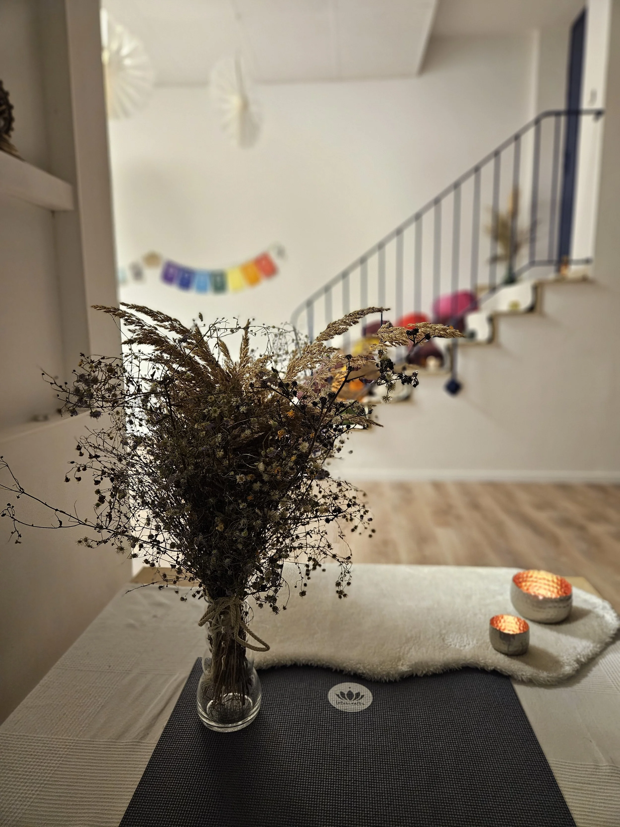 Vase mit getrockneten Blumen auf einem gedeckten Tisch, im Hintergrund eine Treppe, eine Wand mit buntem Wimpelbanner und weißen Papageien-Dekorationen an der Decke.