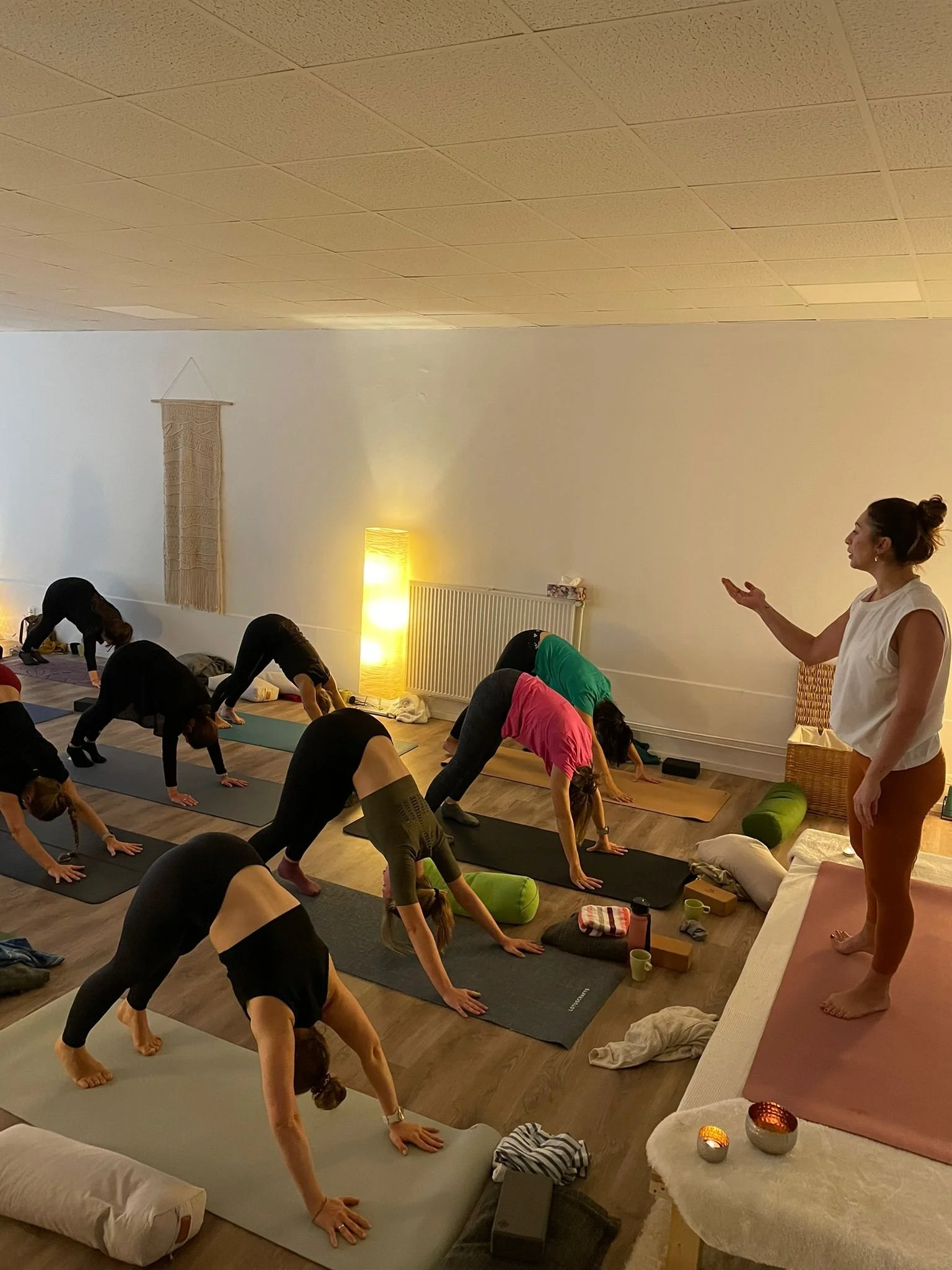 Menschen machen eine Yoga-Klasse in einem ruhigen Raum, angeleitet von einer Frau, die auf einem erhöhten Podest steht.