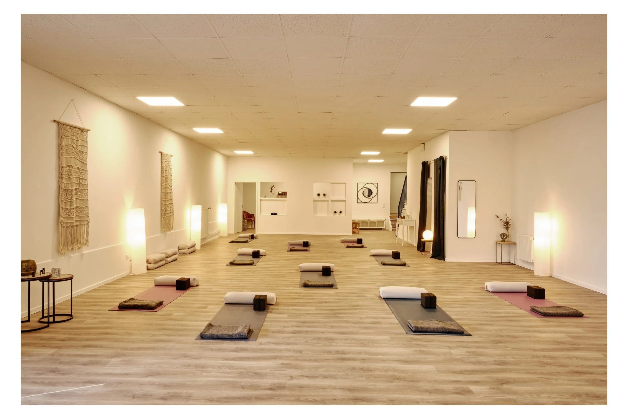 Ein ruhiger Yogaraum mit mehreren Yogamatten, Bolstern und Handtüchern, beige Wanddekorationen und sanfter Beleuchtung.