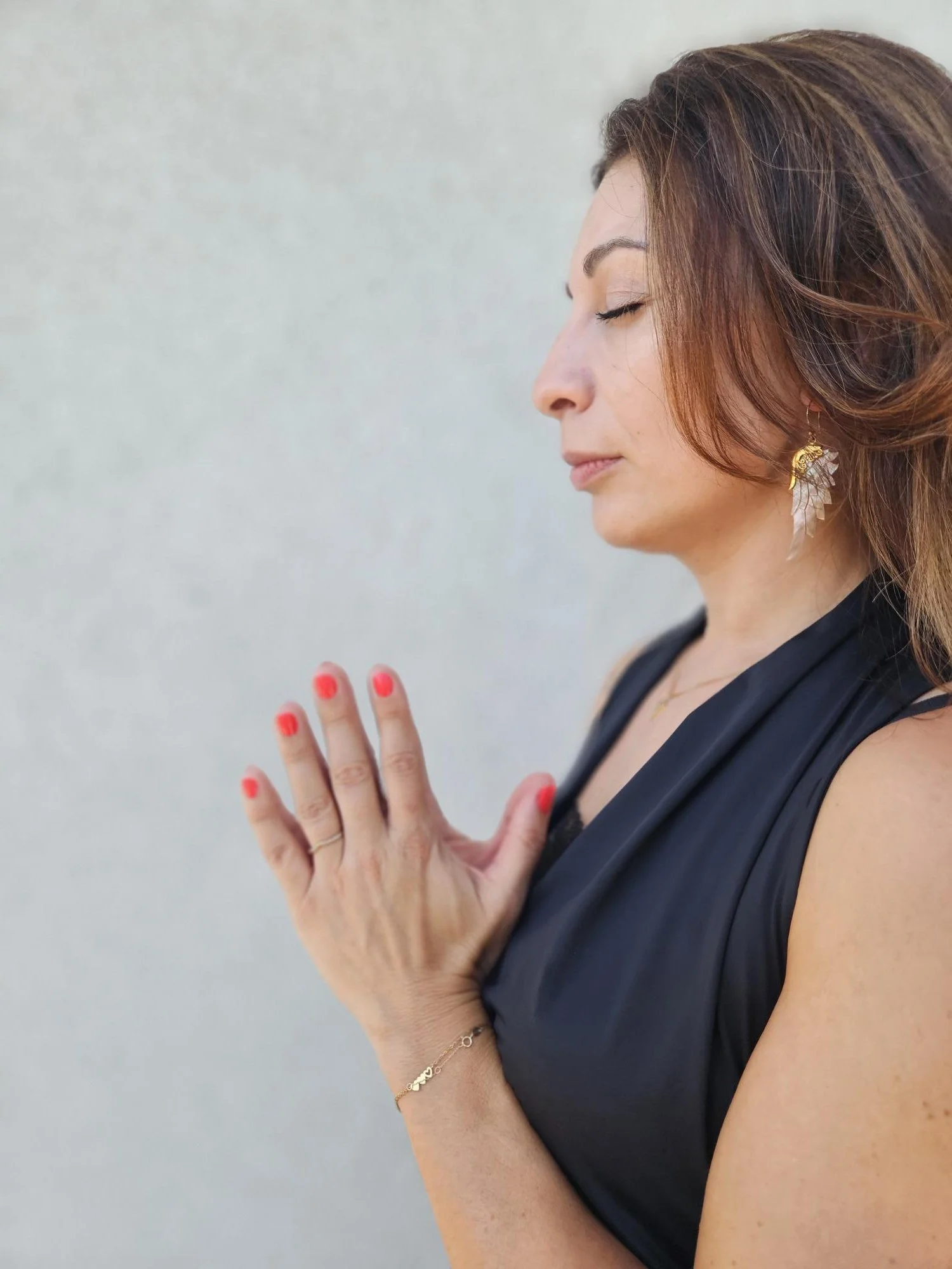 Eine Frau mit roten Haaren, die die Hände vor die Brust gelegt hat, scheint in Meditation oder Gebet zu sein, mit geschlossenen Augen, trägt schwarze Kleidung, goldene Ohrringe und Armbänder.