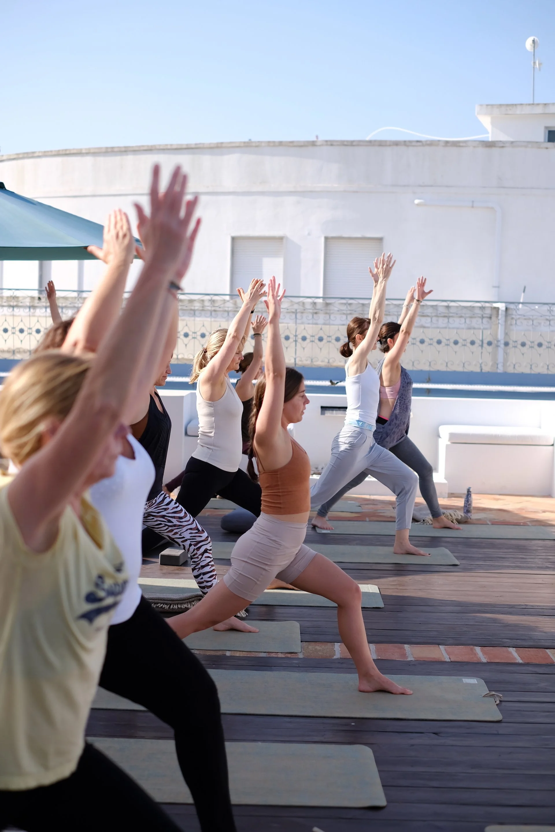 Menschen beim Yoga im Freien auf einem Dach oder einer Terrasse, sie sind in der Baum-Pose und üben Sonnengebet, bei sonnigem Himmel.
