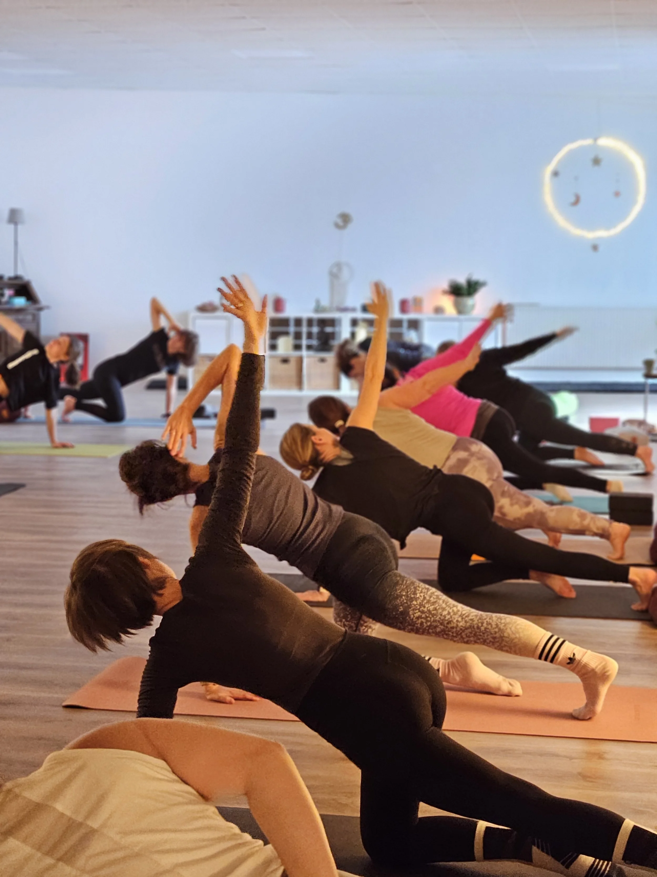 Menschen nehmen an einem Yoga-Kurs in einem hellen, modernen Raum teil, der mit Pflanzen und dekorativen Elementen gestaltet ist.