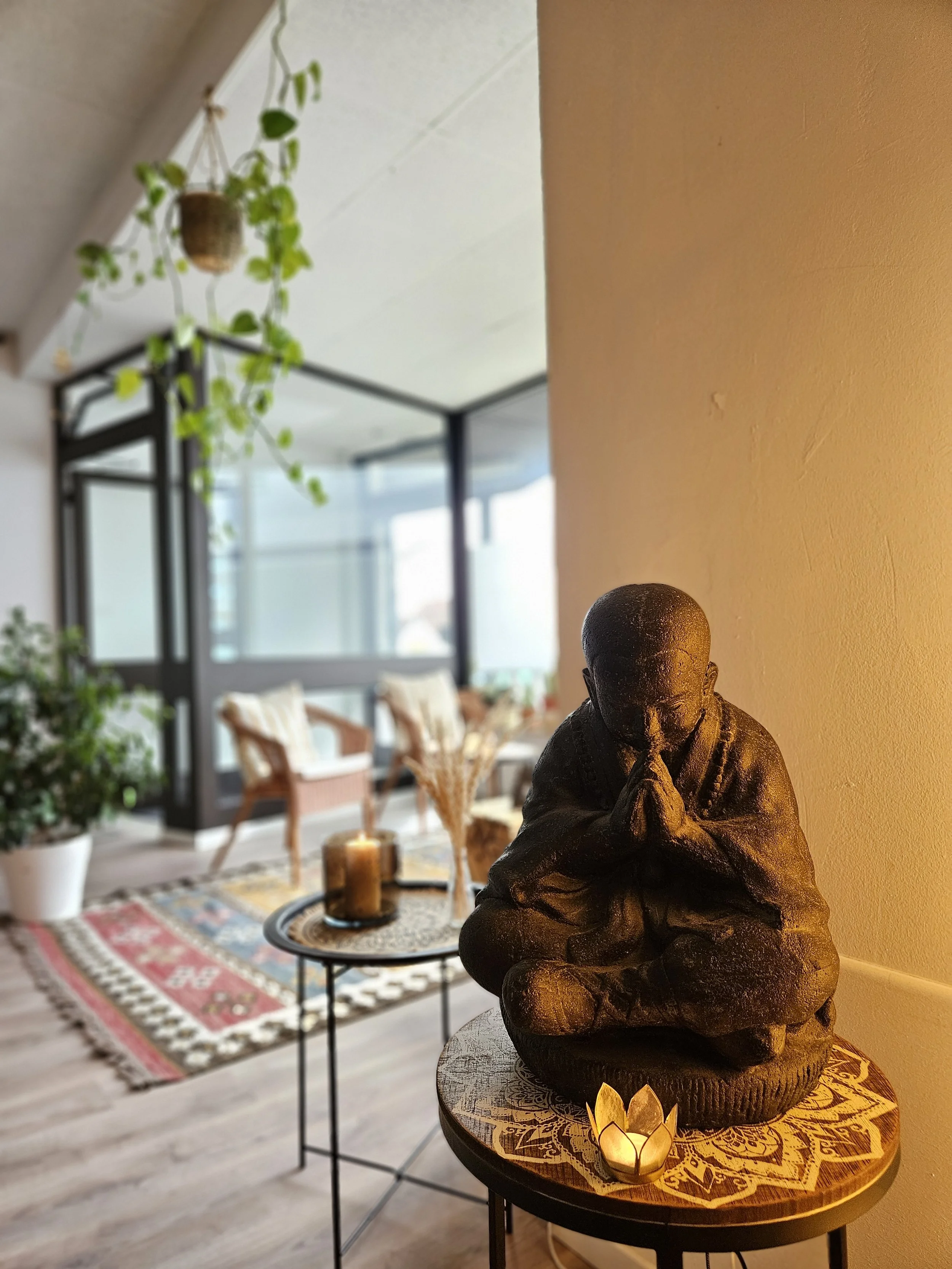 Deko-Figur eines betenden Kindes auf einem runden Tisch mit Lotus-Blüten-Teelicht in einem gemütlichen Raum mit Pflanzen und Sitzbereich.