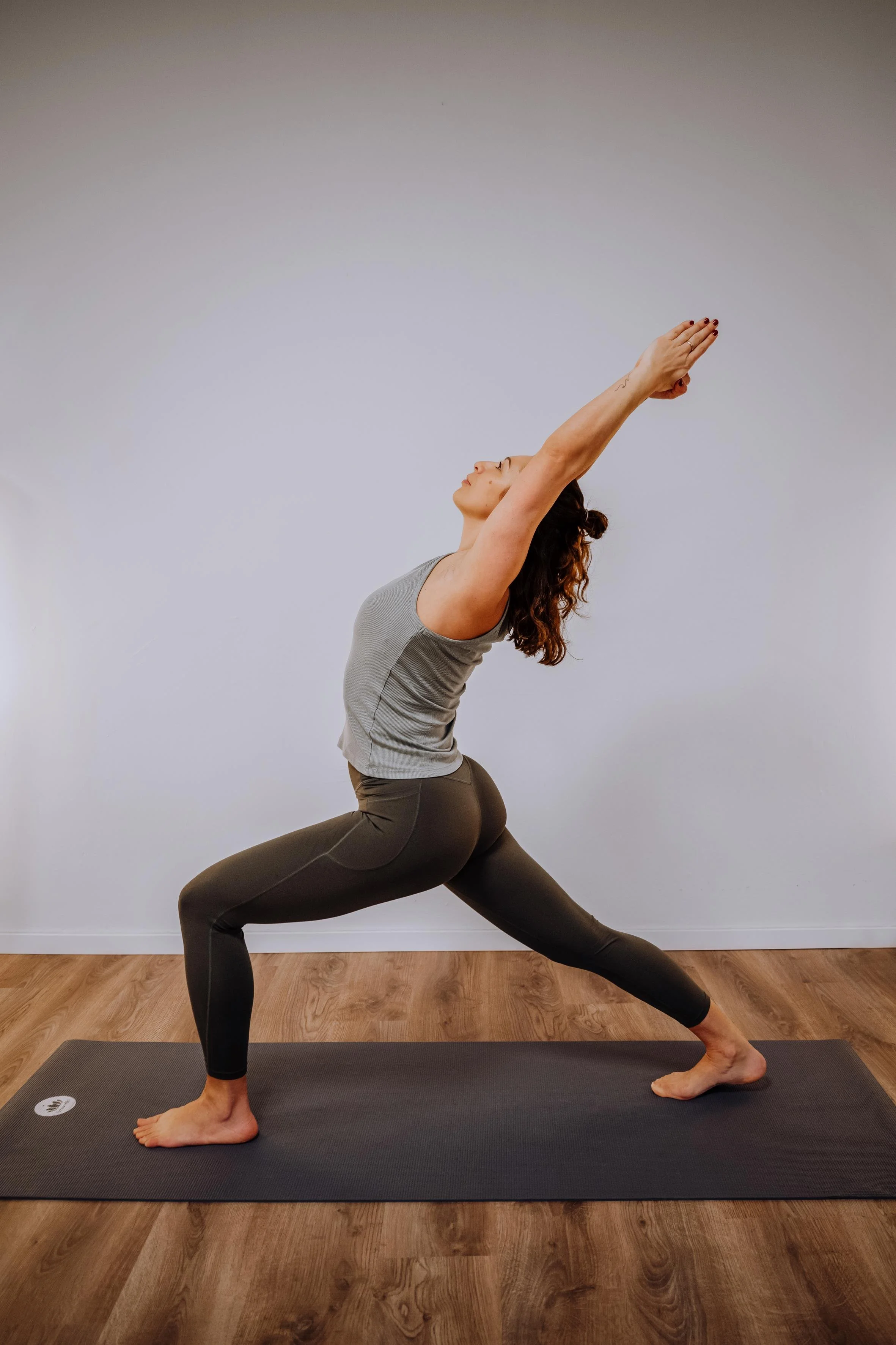 Frau beim Yoga in einer tiefen Kriegerposition auf einer Yogamatte in einem Raum mit Holzfußboden.