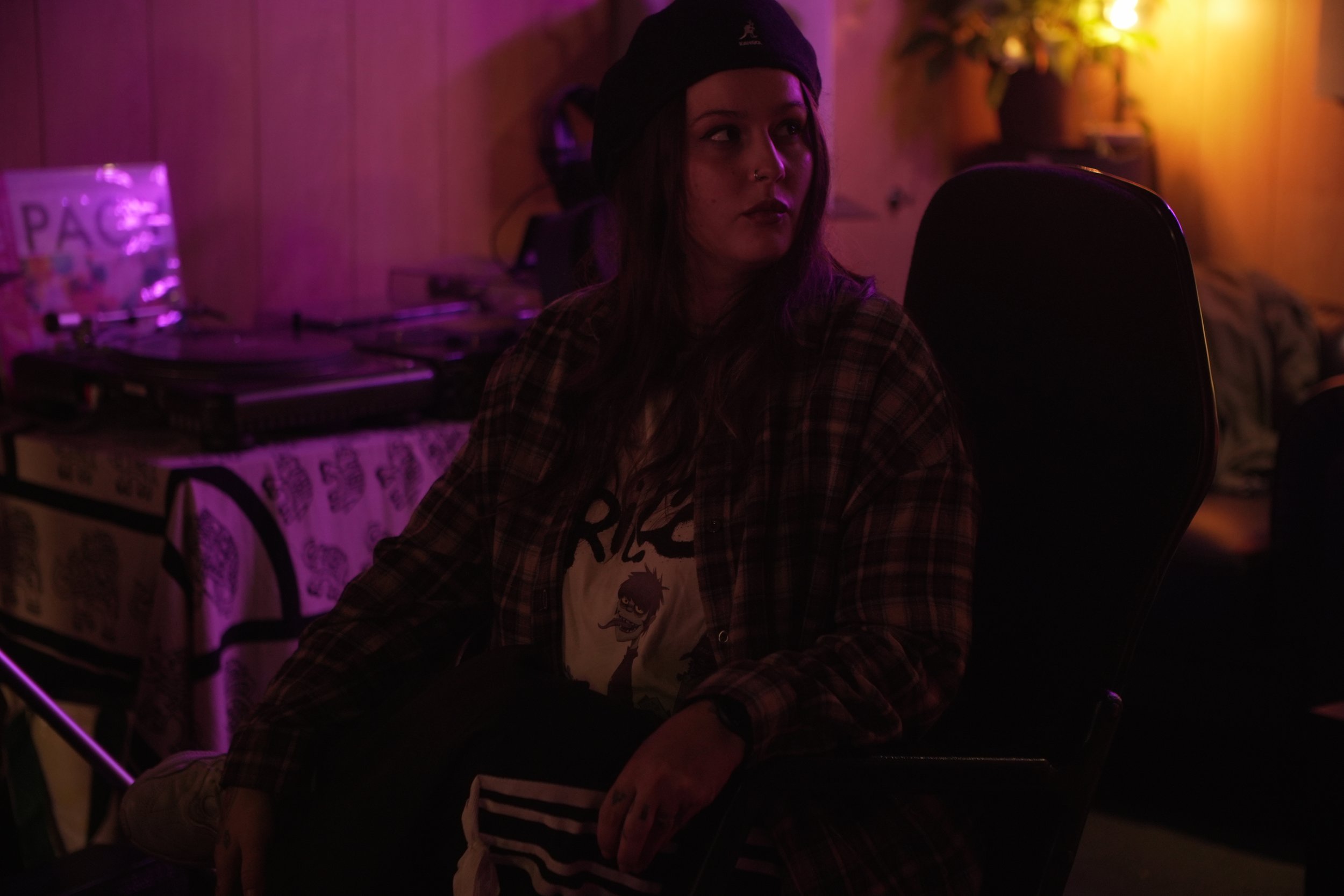 Una mujer sentada en una silla en un ambiente con iluminación tenue y colores cálidos, probablemente en un estudio o una sala de conciertos.