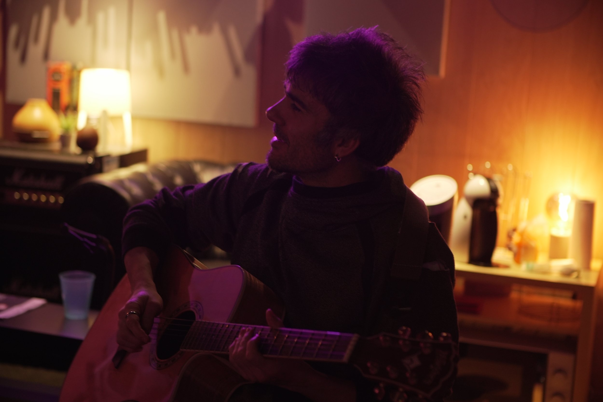 Persona tocando la guitarra en un ambiente con iluminación cálida y ambiente íntimo.