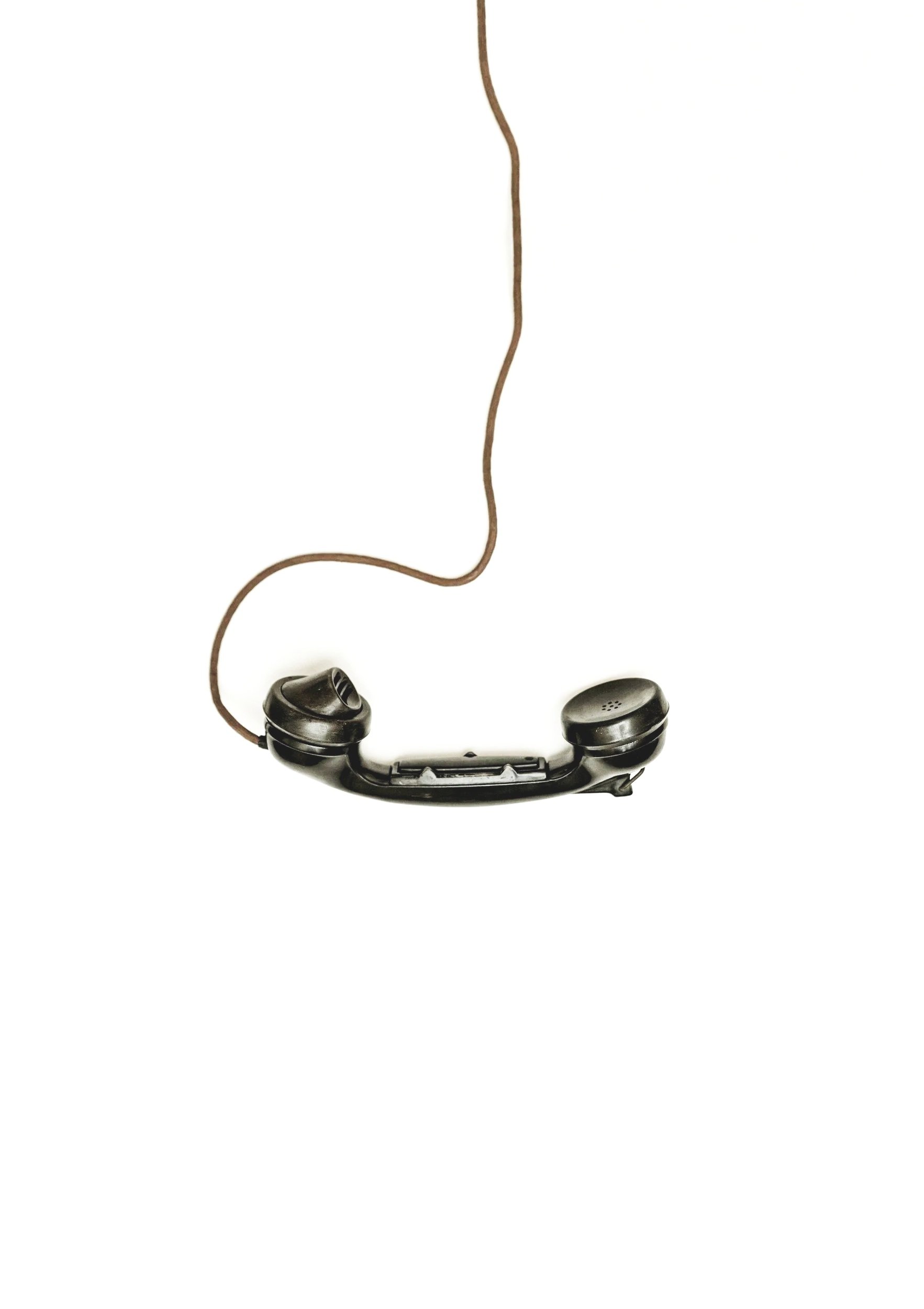 A black vintage rotary phone with a long, thin brown cord on a white background.