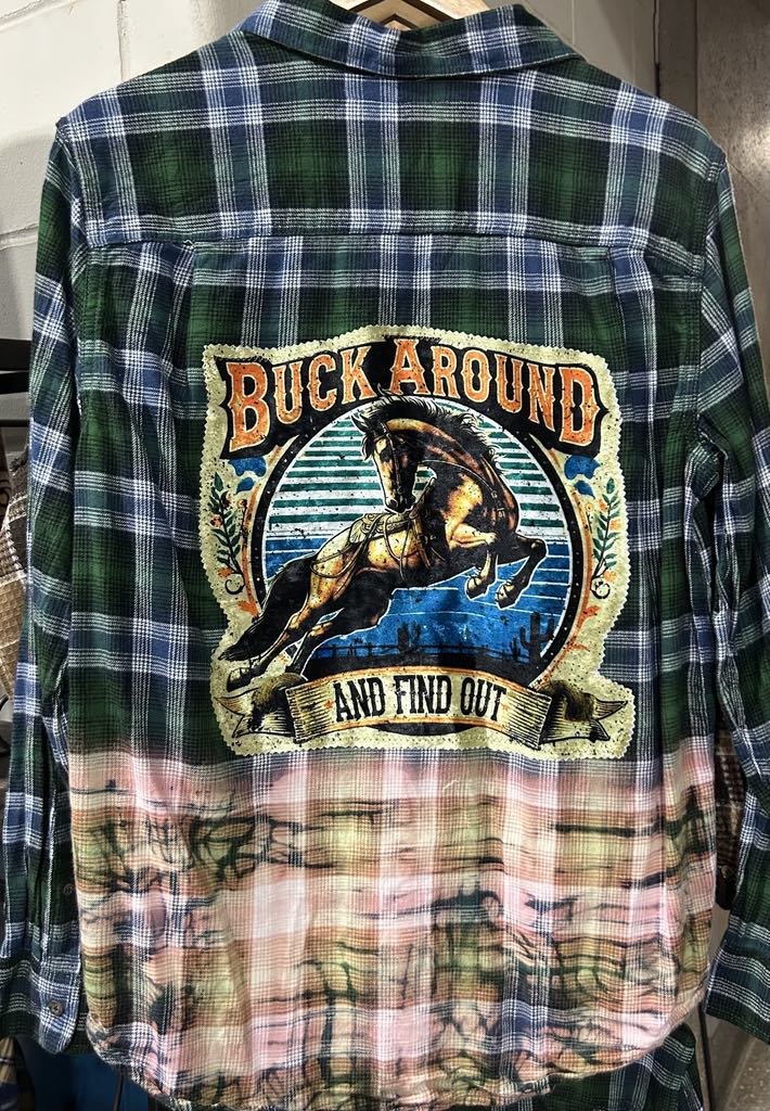 Plaid shirt with a large embroidered patch on the back featuring a horse jumping over a fence and text that reads 'Buck Around and Find Out'.