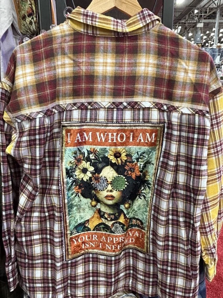 Plaid shirt with a colorful patch featuring an artistic portrait of a woman with flowers in her hair, wearing sunglasses, and the text "I AM WHO I AM" and "YOUR APPROVAL ISN'T NEEDED".