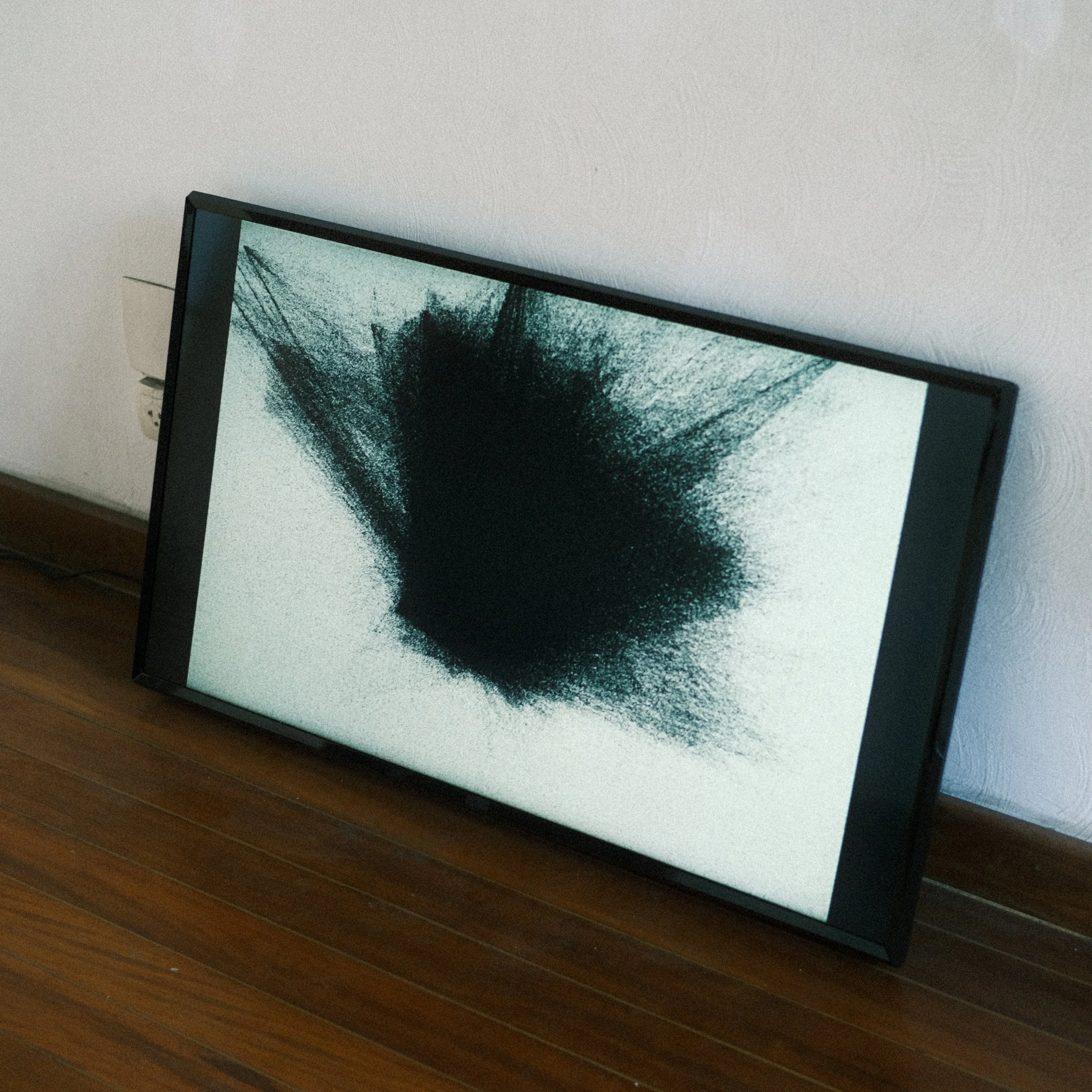 Tela de televisão exibindo uma imagem abstrata preta e branca, apoiada no chão de madeira e encostada na parede.