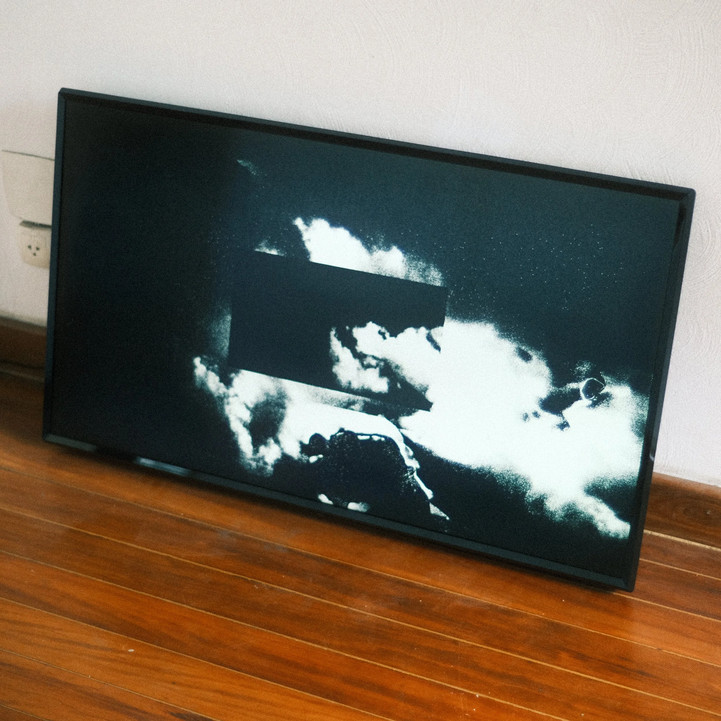 Tela de televisão com uma imagem em preto e branco de nuvens no céu e um objeto escuro no centro.