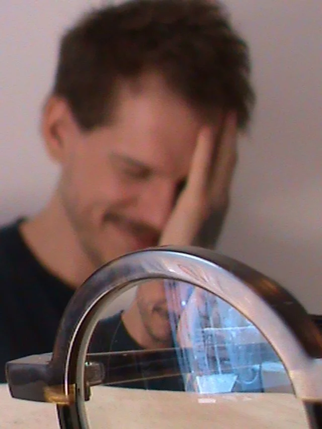 Homem com mão no rosto, foto de perfil. Atrás do óculos.