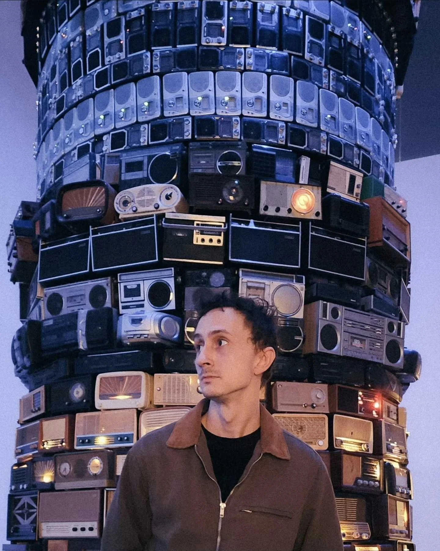 Dylan standing in front of a tower of retro stereos and radios with a blue and orange tint.
