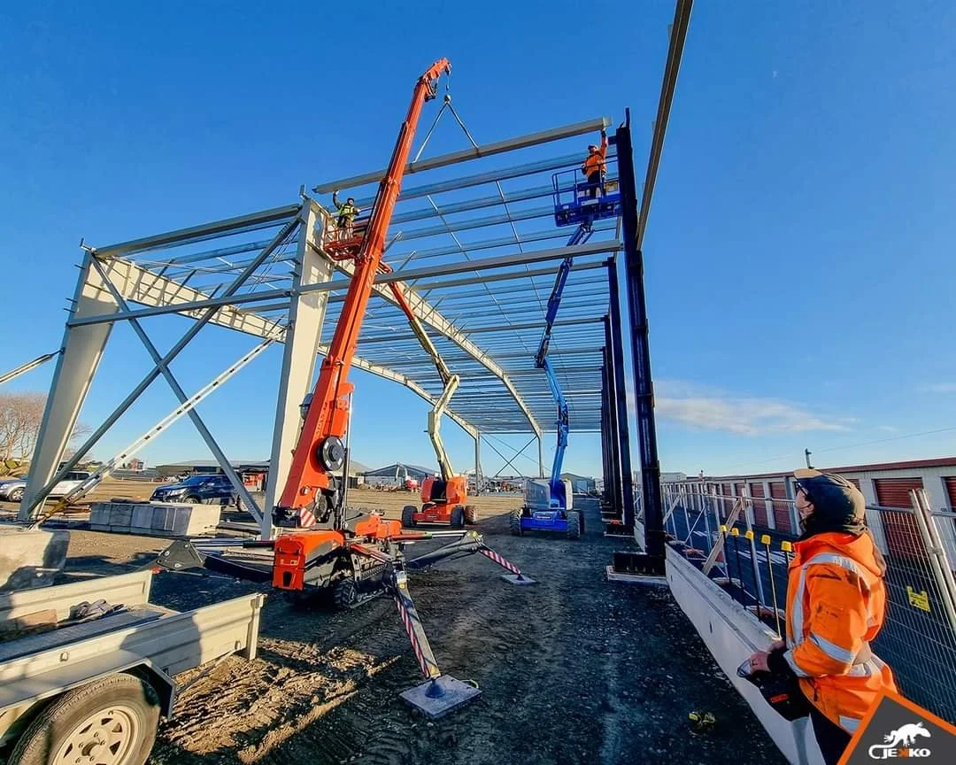 Construction workers building a metal structure with cranes and lifts at a construction site.