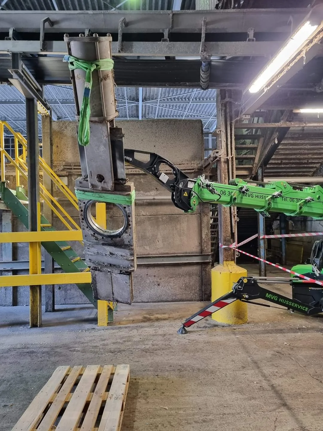 Industrial scene with robotic arm lifting a large, rusted metal piece in a factory or warehouse.