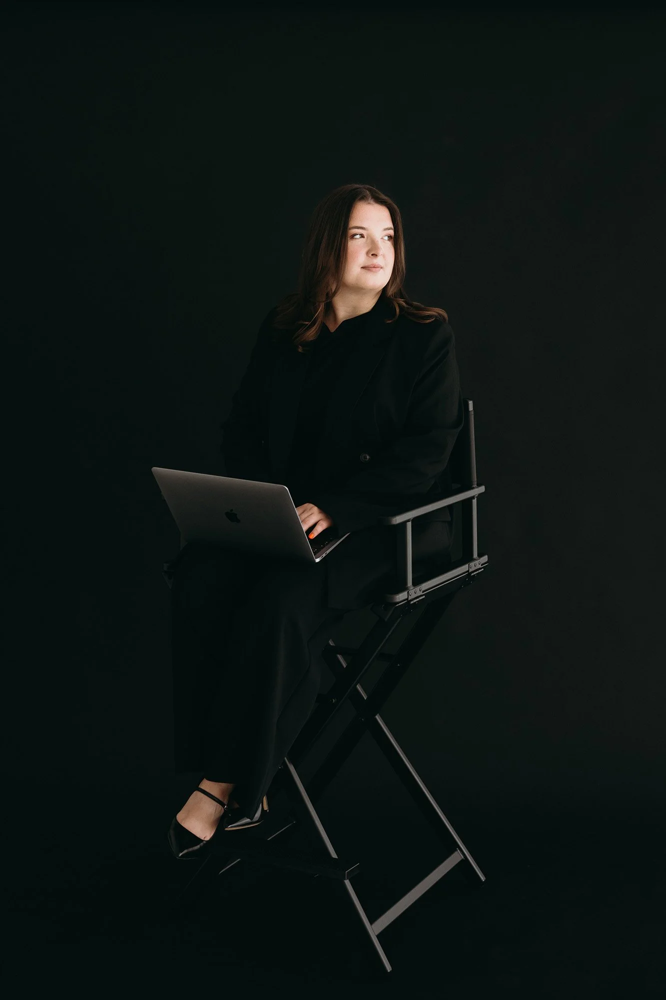 A woman sat on a black chair in a dark room quietly showing confidence in the Build It client system and ready to work