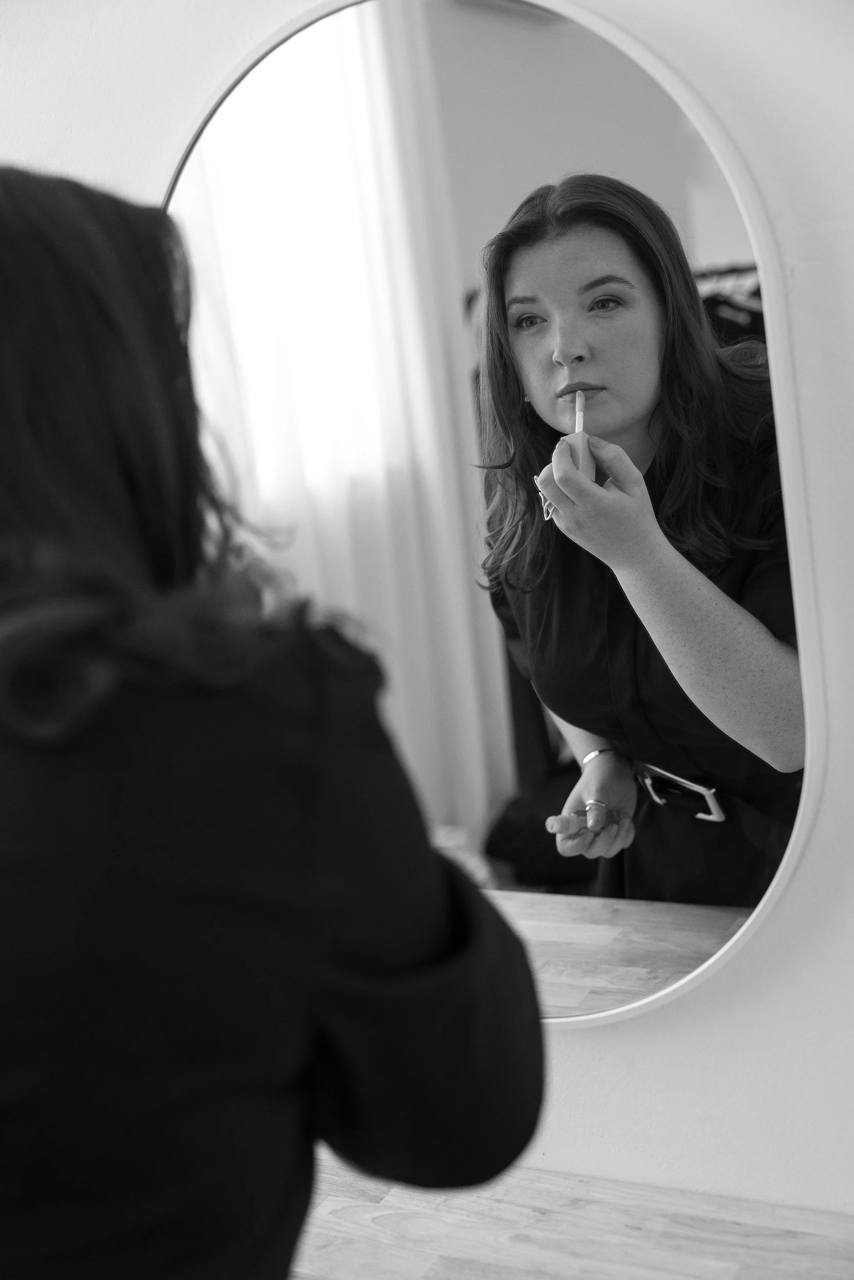 Lauren, Founder of Unravel, is applying lipstick while looking in a mirror.