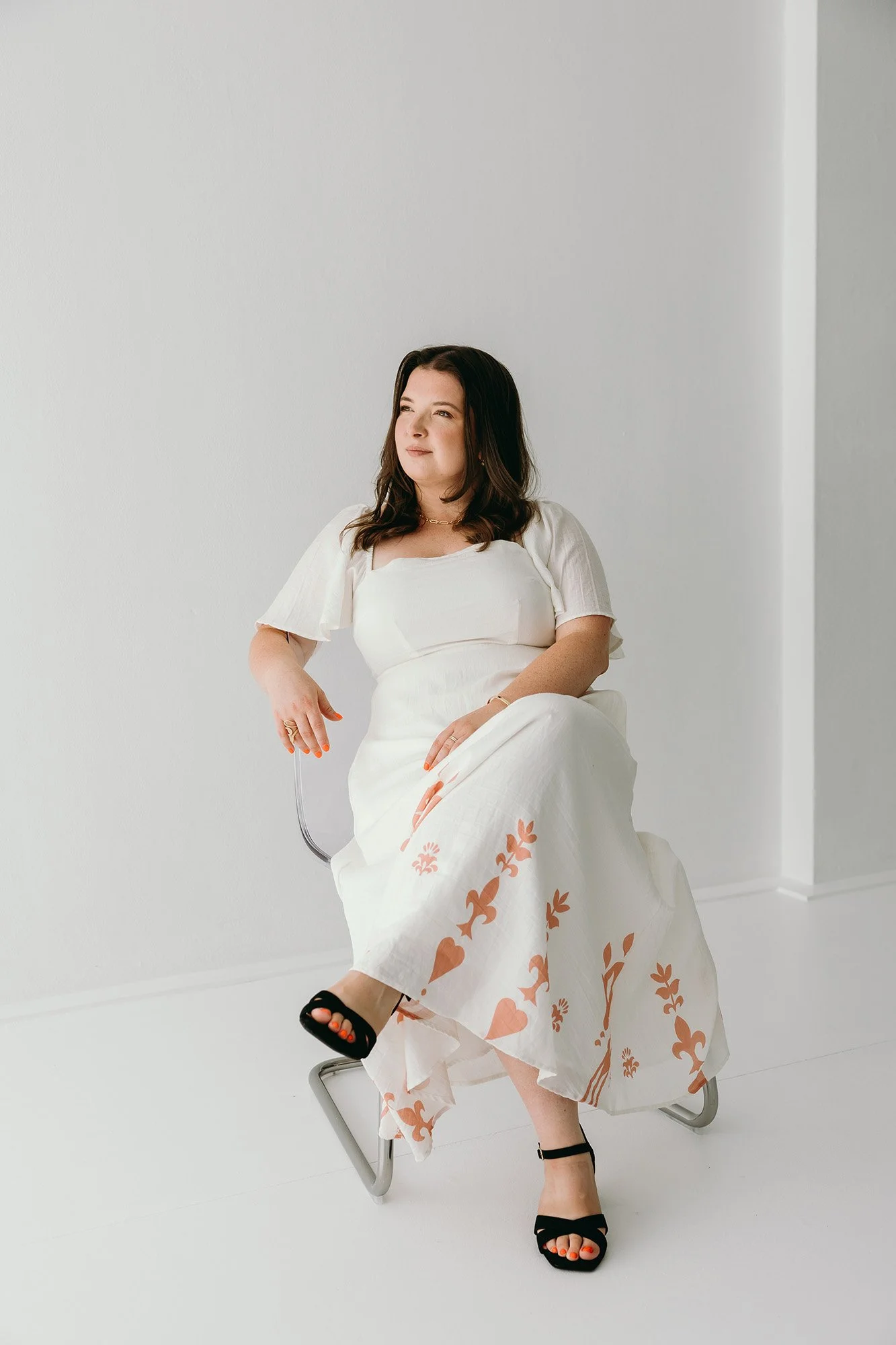 Lauren Hunter of Unravel sitting in a chair and a white dress with orange patterns to show her business values