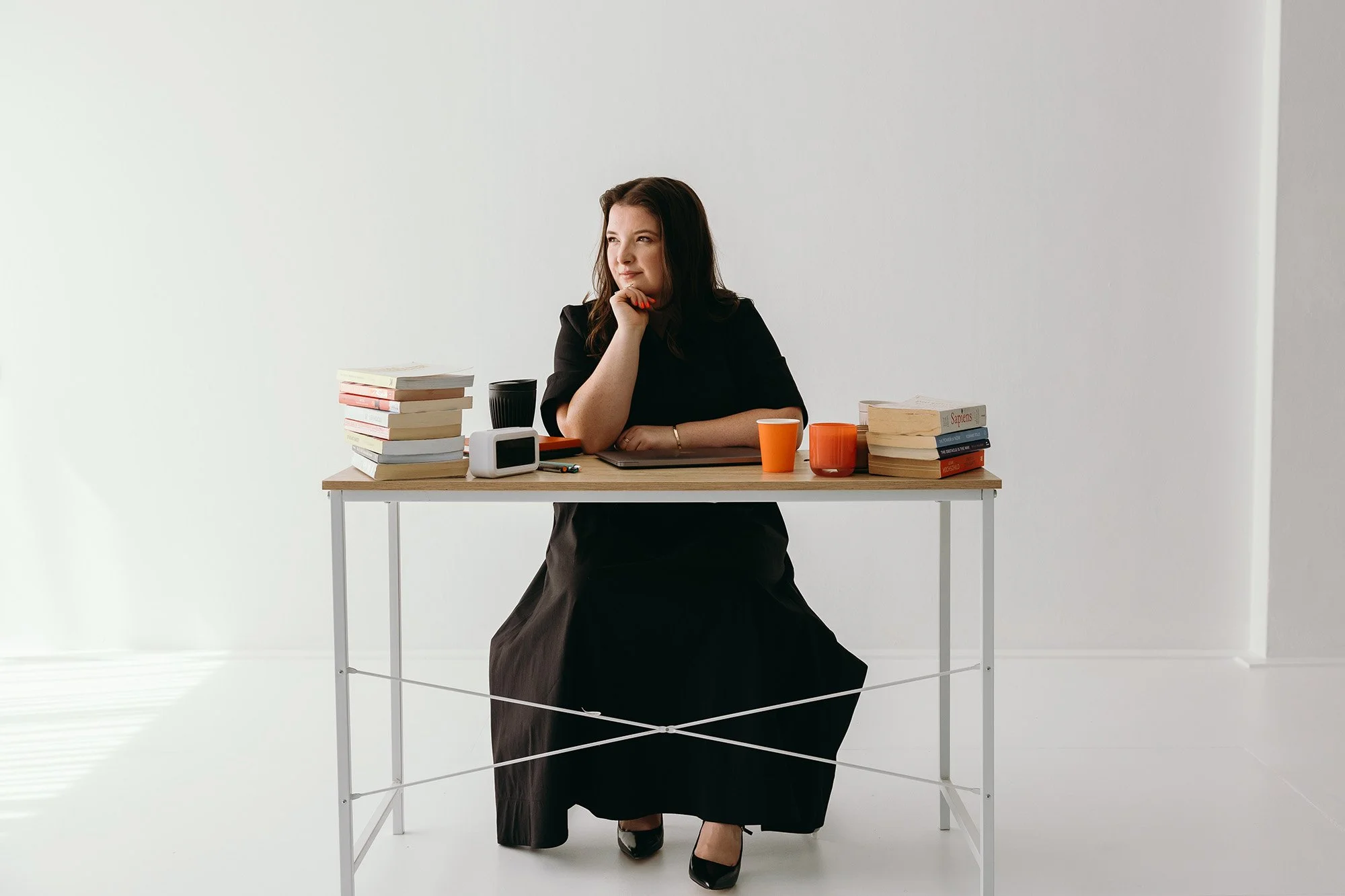 Lauren Hunter, Unravel business systems consultant, seated thoughtfully at a desk surrounded by stacks of books, coffee cups, and a laptop, reflecting her knowledgeable and approachable consulting style.