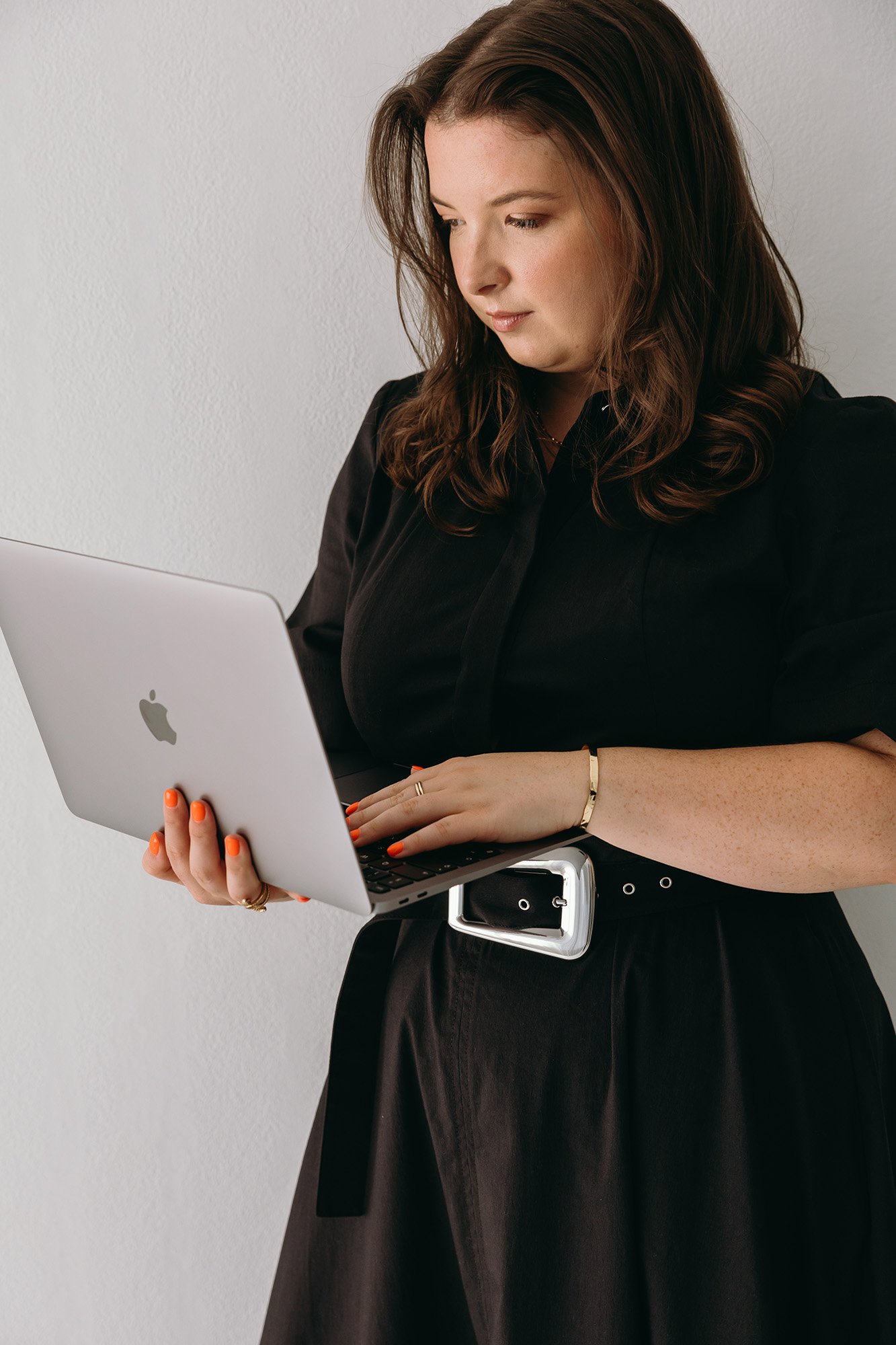 Lauren in a black dress holds an open laptop while reviewing her work, representing Unravel's hands-on approach to setting up client systems, emails, and funnels through 1 to 1 support.
