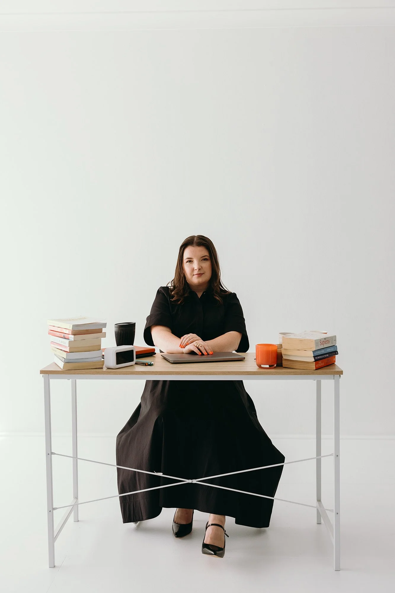 Lauren, Founder of Unravel, is sitting at a desk with books, coffee cup, and office supplies in front of a plain white background.