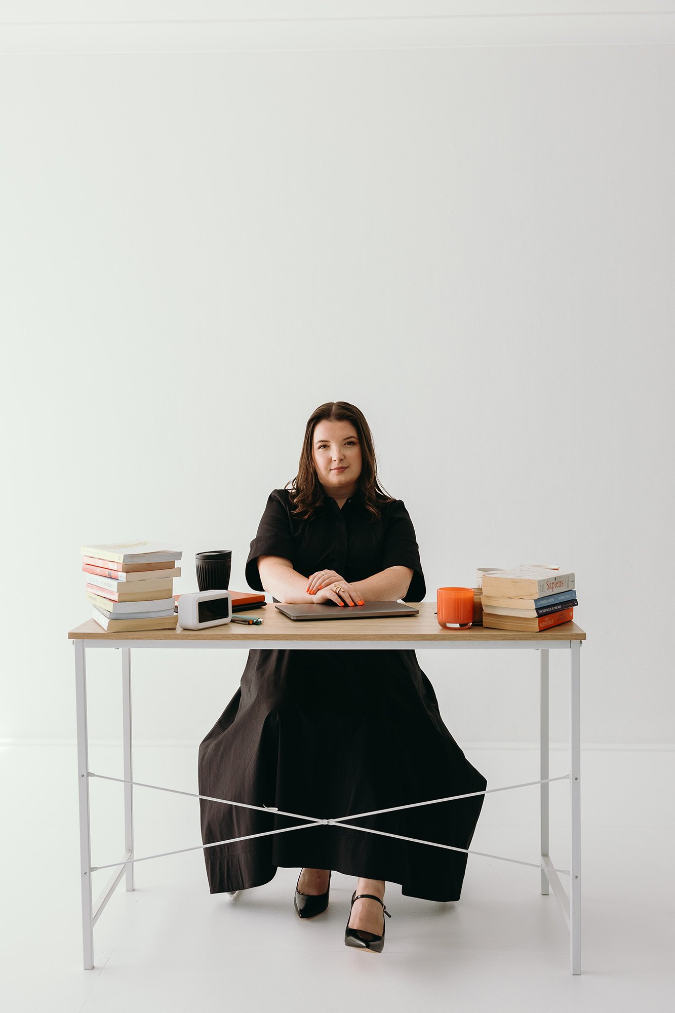 Lauren Hunter, founder of Unravel, confidently sitting at her desk with a MacBook, stack of books, and coffee cups, with a blank wall behind her showing readiness to get to work.