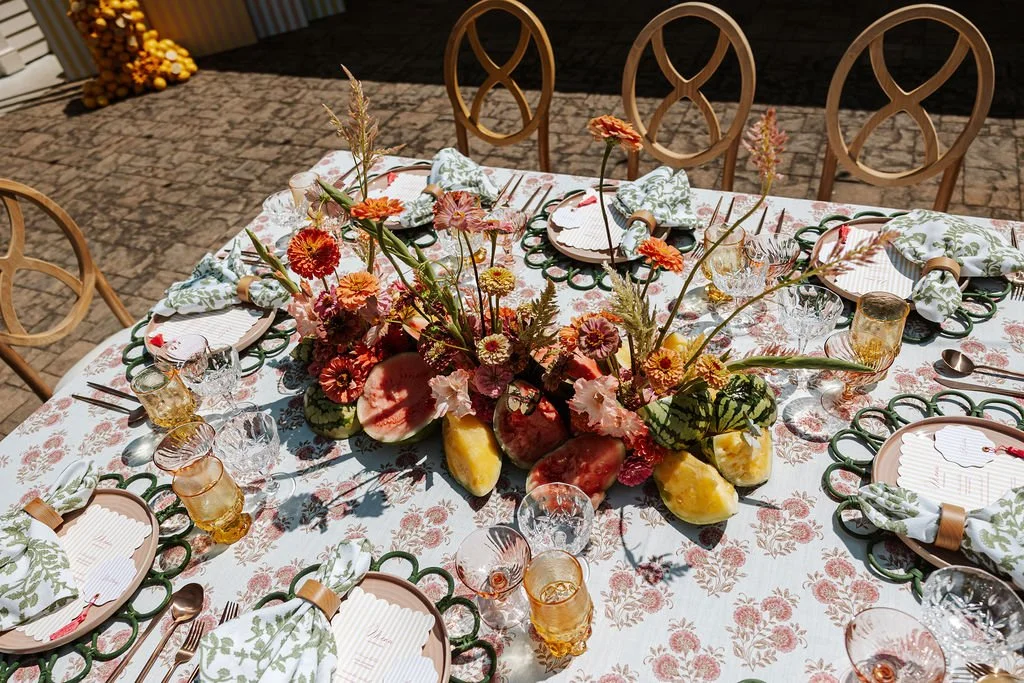 A decorated dining table with a floral centerpiece, place settings, and glassware, set for a meal in a well-lit room.