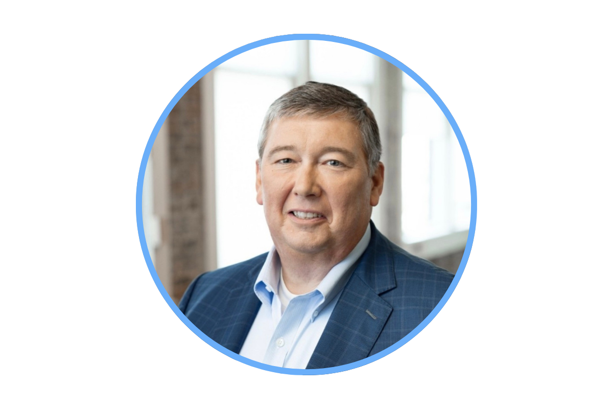 Headshot of a middle-aged man in a blue suit smiling, with a blurred office background.