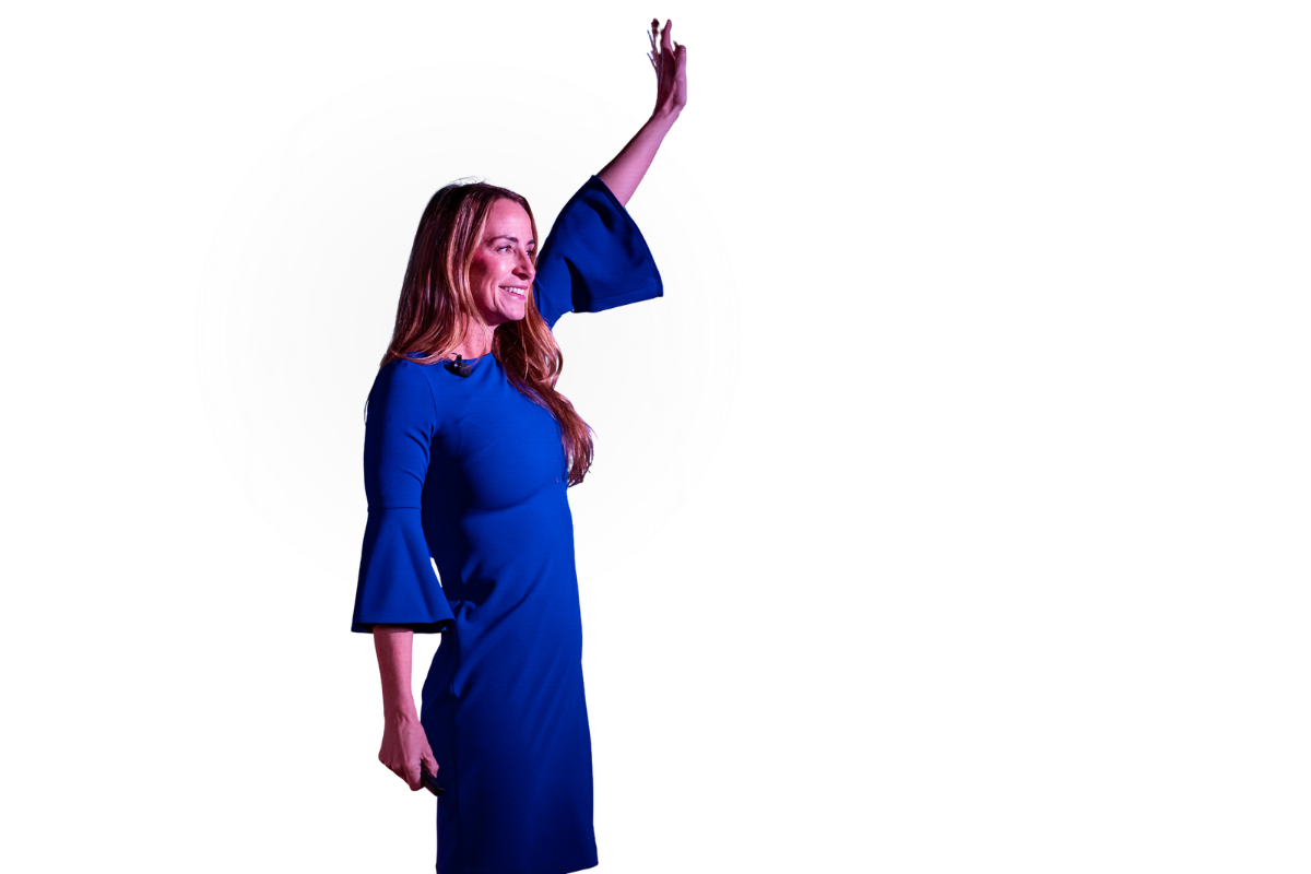 A woman wearing a blue dress waving with her right hand, standing in front of a white circular background with concentric rings.