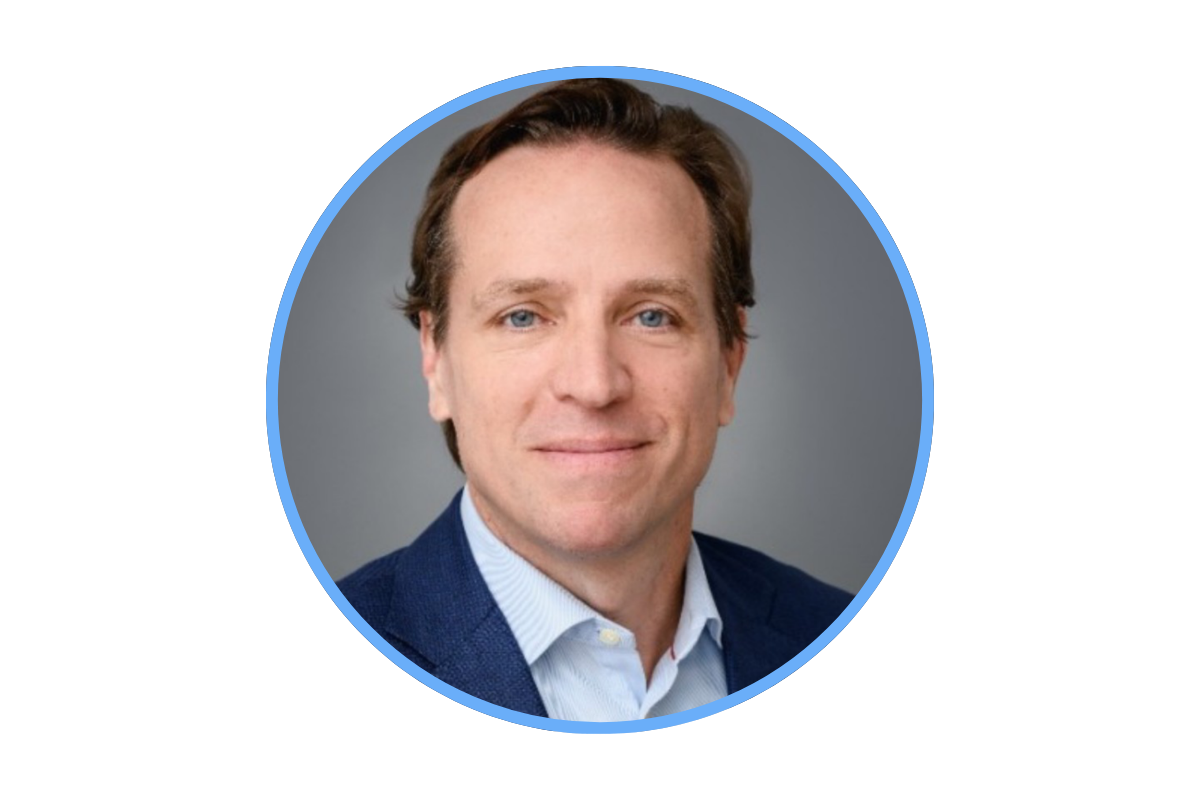 Professional headshot of a man with brown hair in a blue suit and light blue shirt, smiling against a gray background.