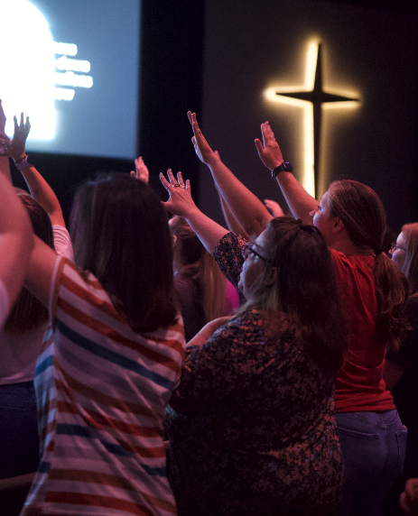 People worshiping in a church with hands raised, illuminated cross on the wall