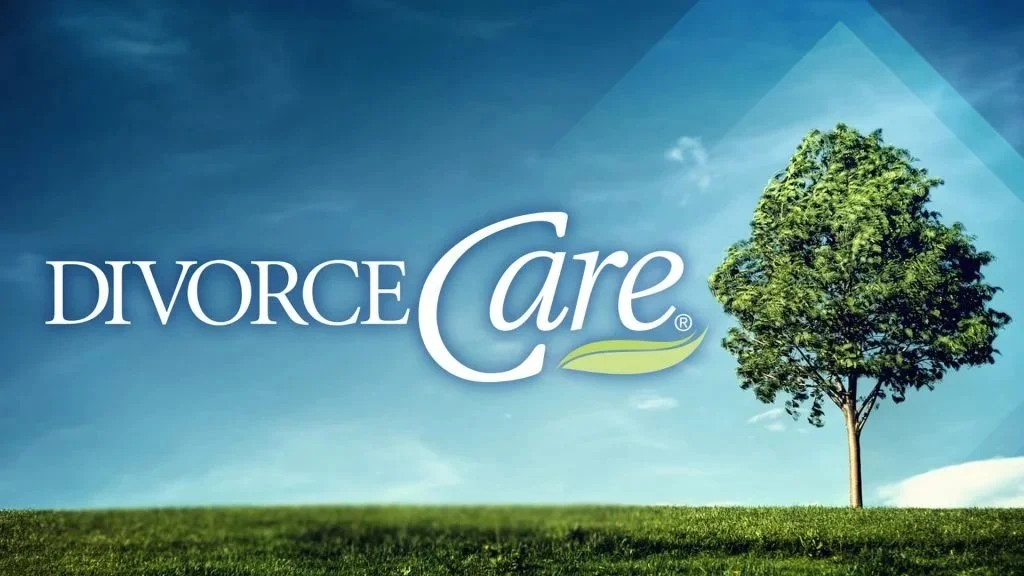 A logo with the words 'Divorce Care' on a grassy field with a single tree and blue sky with clouds in the background.