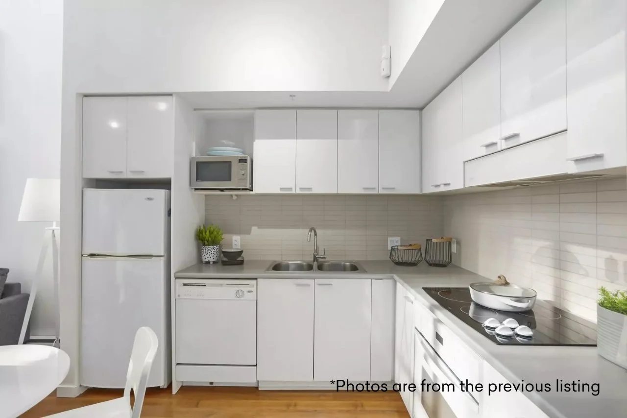 White kitchen with upper and lower cabinets, a dishwasher, refrigerator, microwave, stovetop, and sink. Decor includes potted plants and baskets.