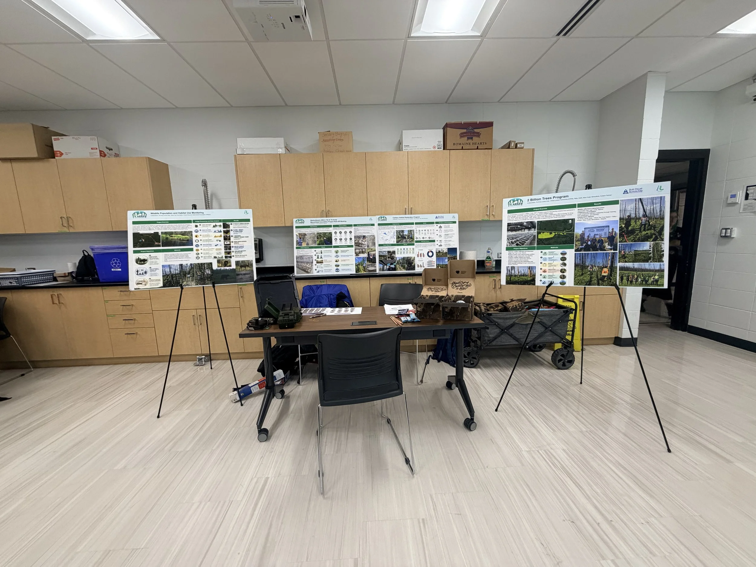 TK Array display at NAIT’s career fair, featuring posters about wildlife monitoring, caribou habitat restoration, and the 2 Billion Trees Program, with field equipment on a table.