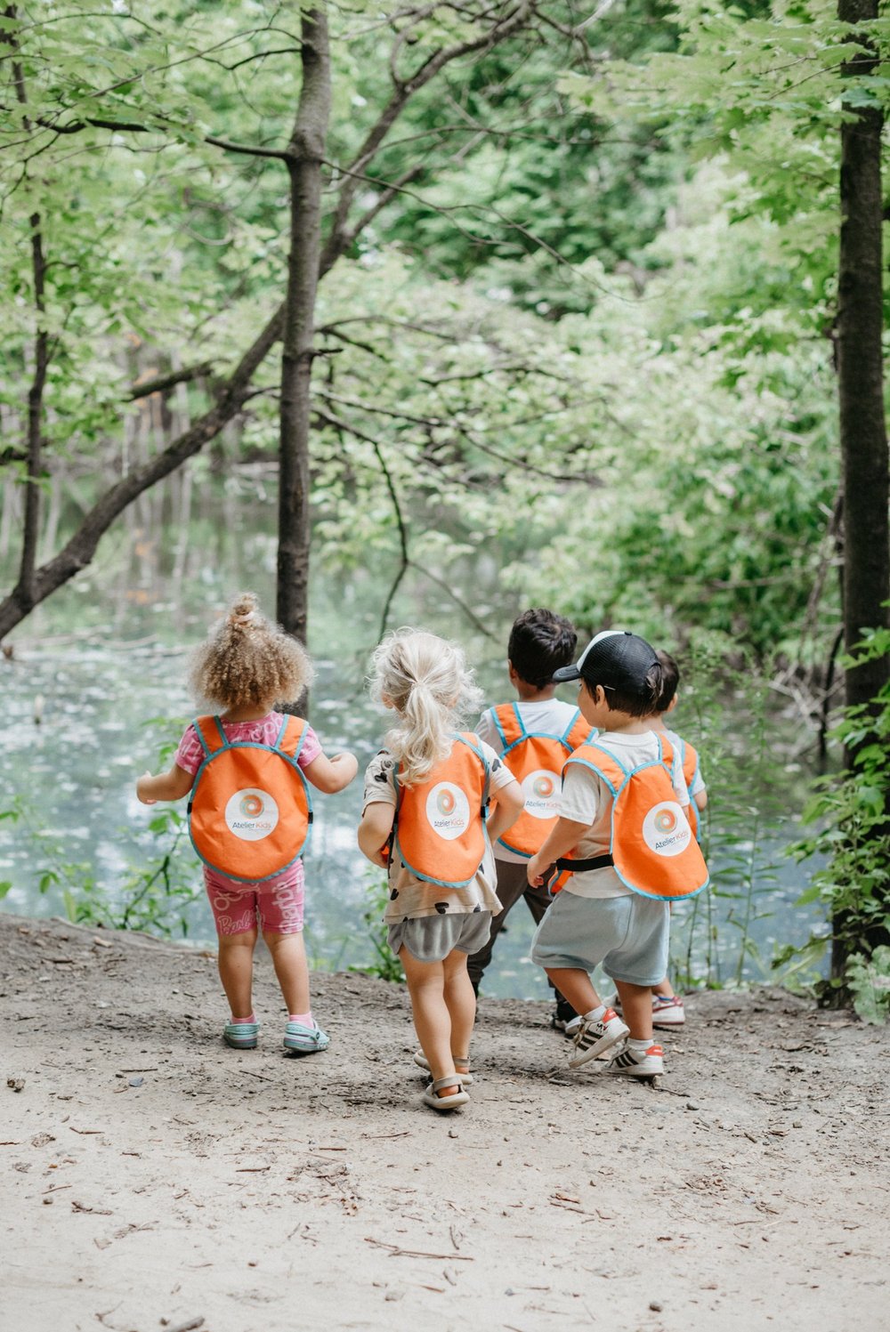 Children with orange backpacks exploring a wooded trail together.