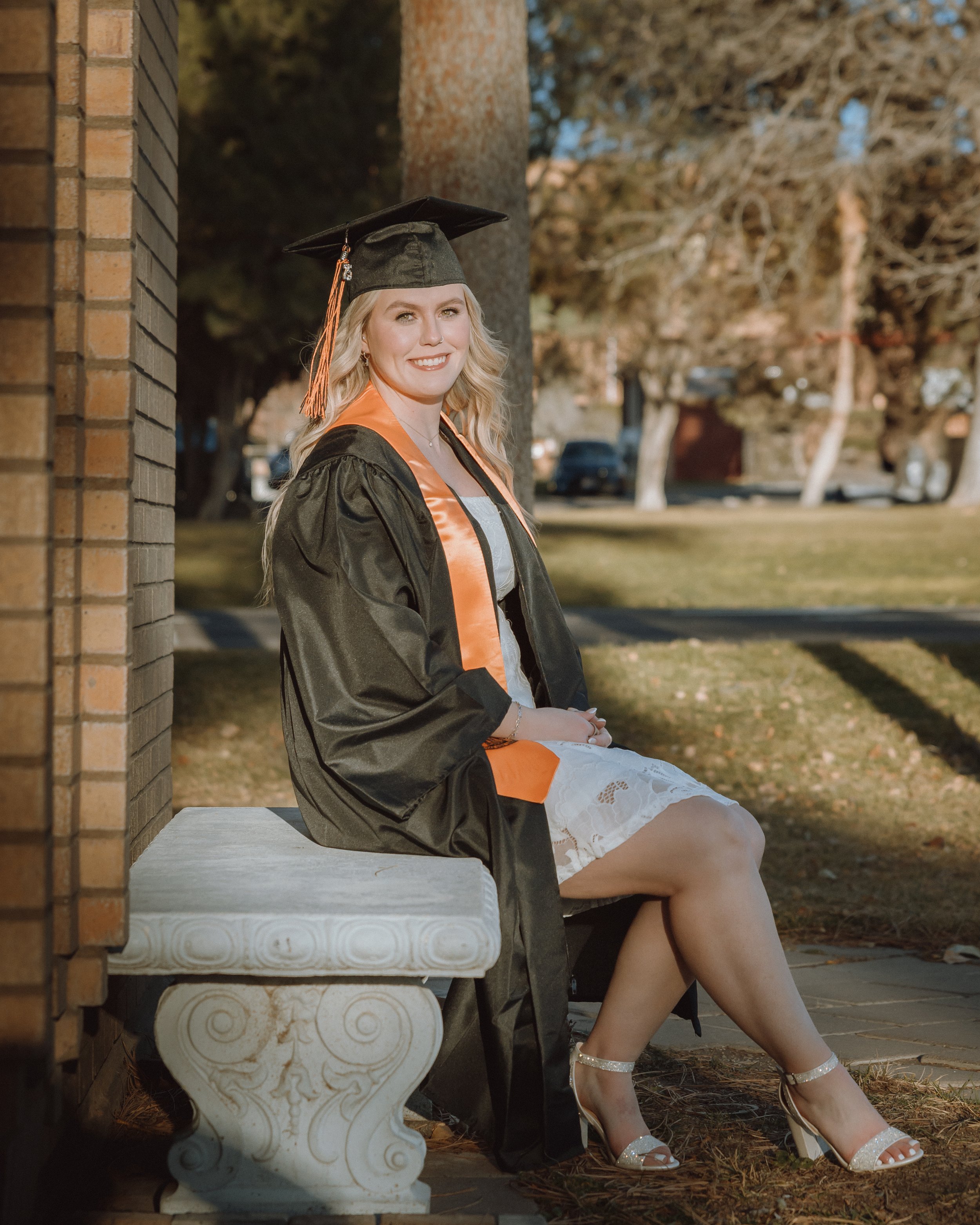 women sitting on the bench on campus at isu taking graduation photos in her cap and gown