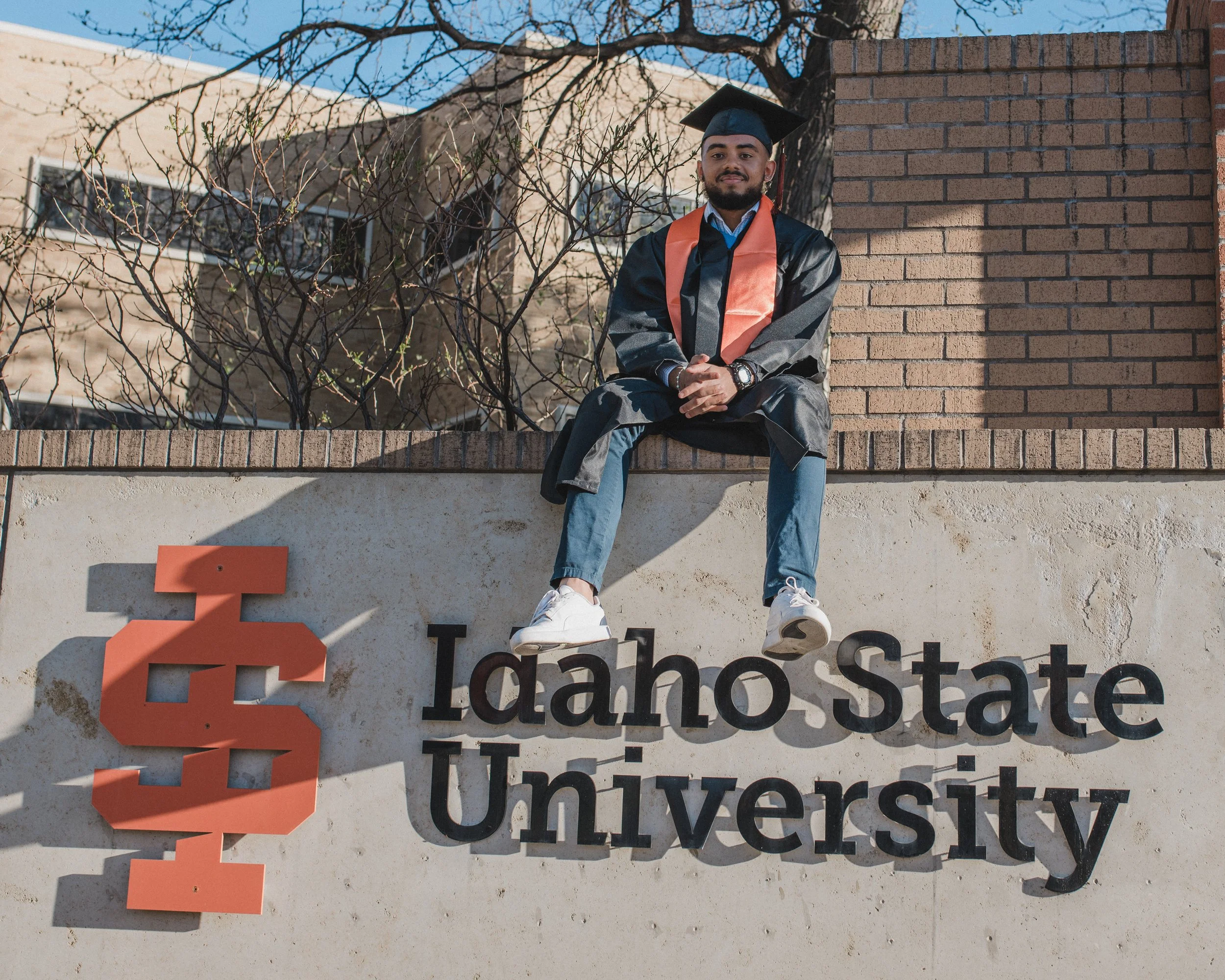 man sitting on the idaho state university sign at isu graduation