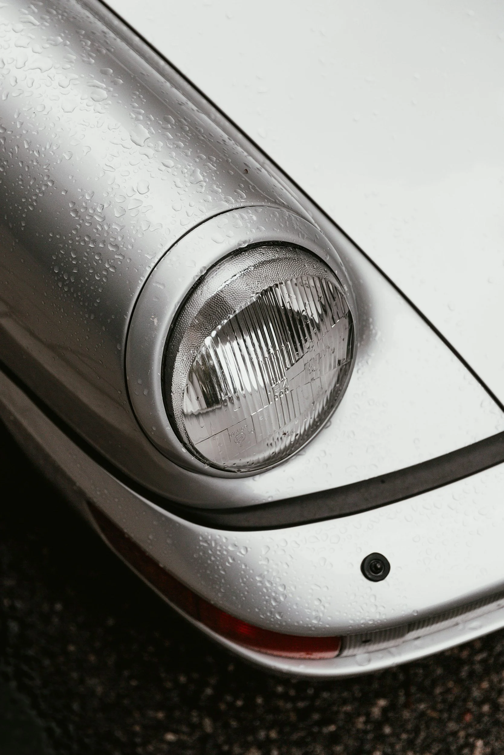 Close-up of a wet, silver car headlight with droplets of water on the surface.