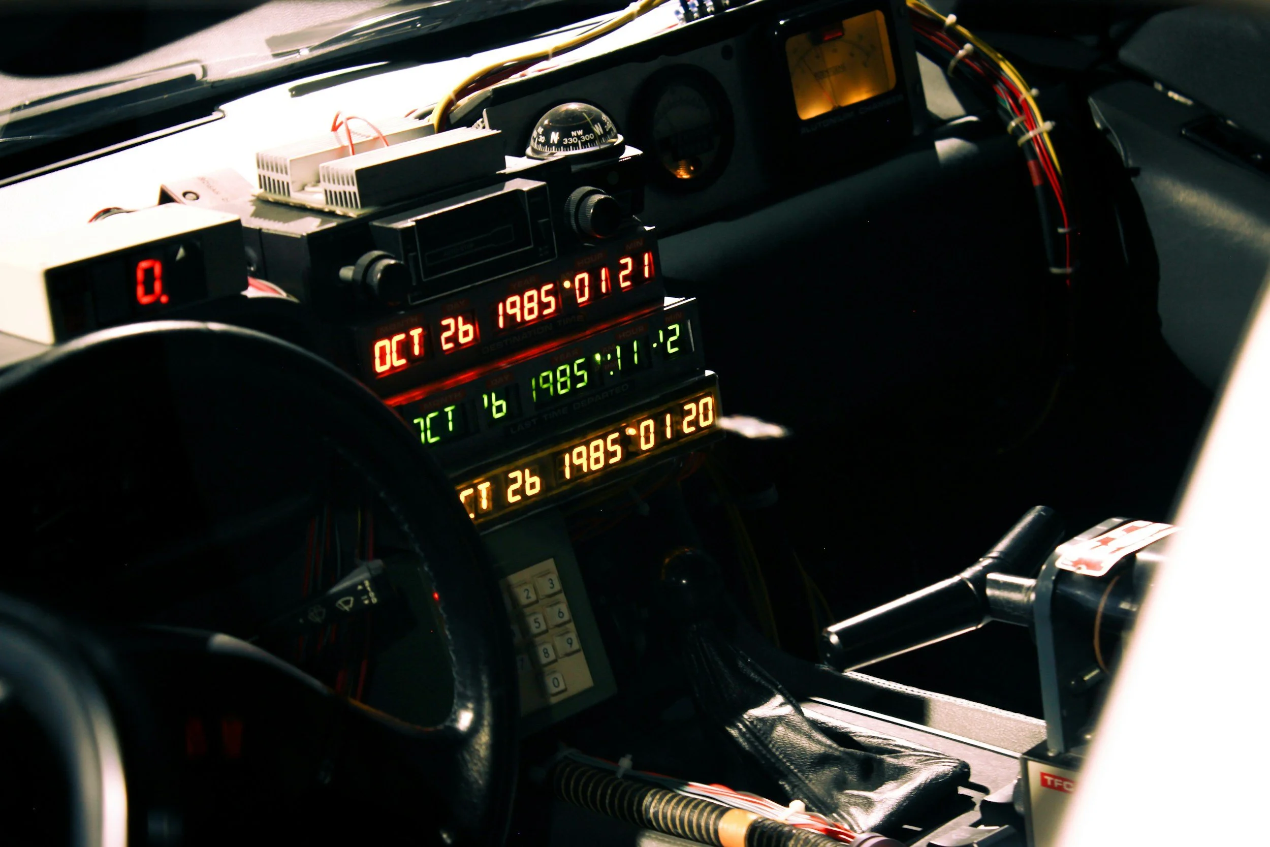 Inside view of a Delorean DMC 12 with digital displays showing dates, times, and other data, as well as a steering wheel and gear shift. Restore a DeLoren with Capital Conversion in NJ or swap the motor with an electric motor and make it an EV.