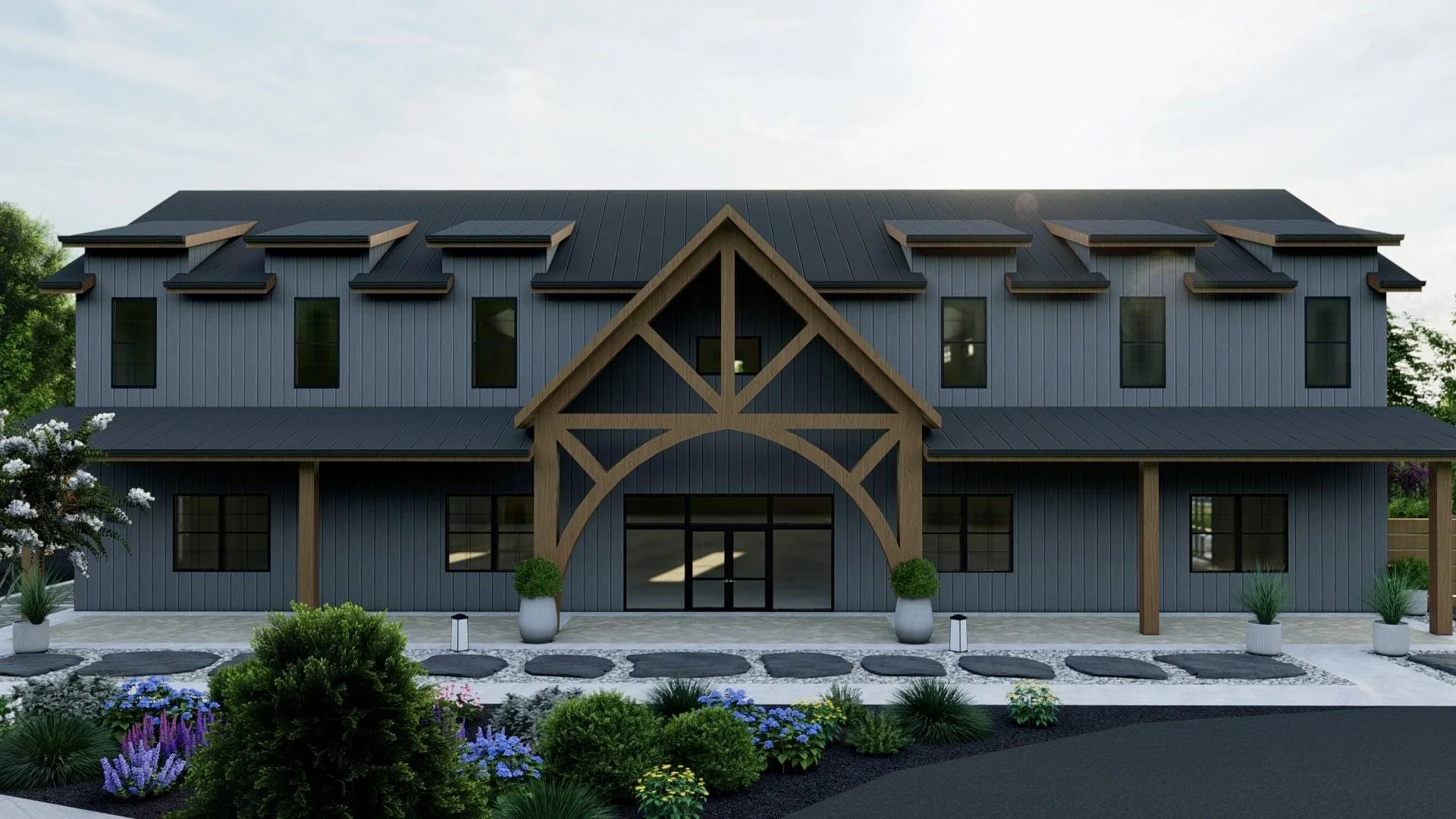 A modern two-story building with gray vertical siding, black roof, and wooden trim. The entrance is framed by large wooden beams forming a decorative arch with small potted plants on either side. The front yard features landscaped plants, flowers, and a walkway with stepping stones.