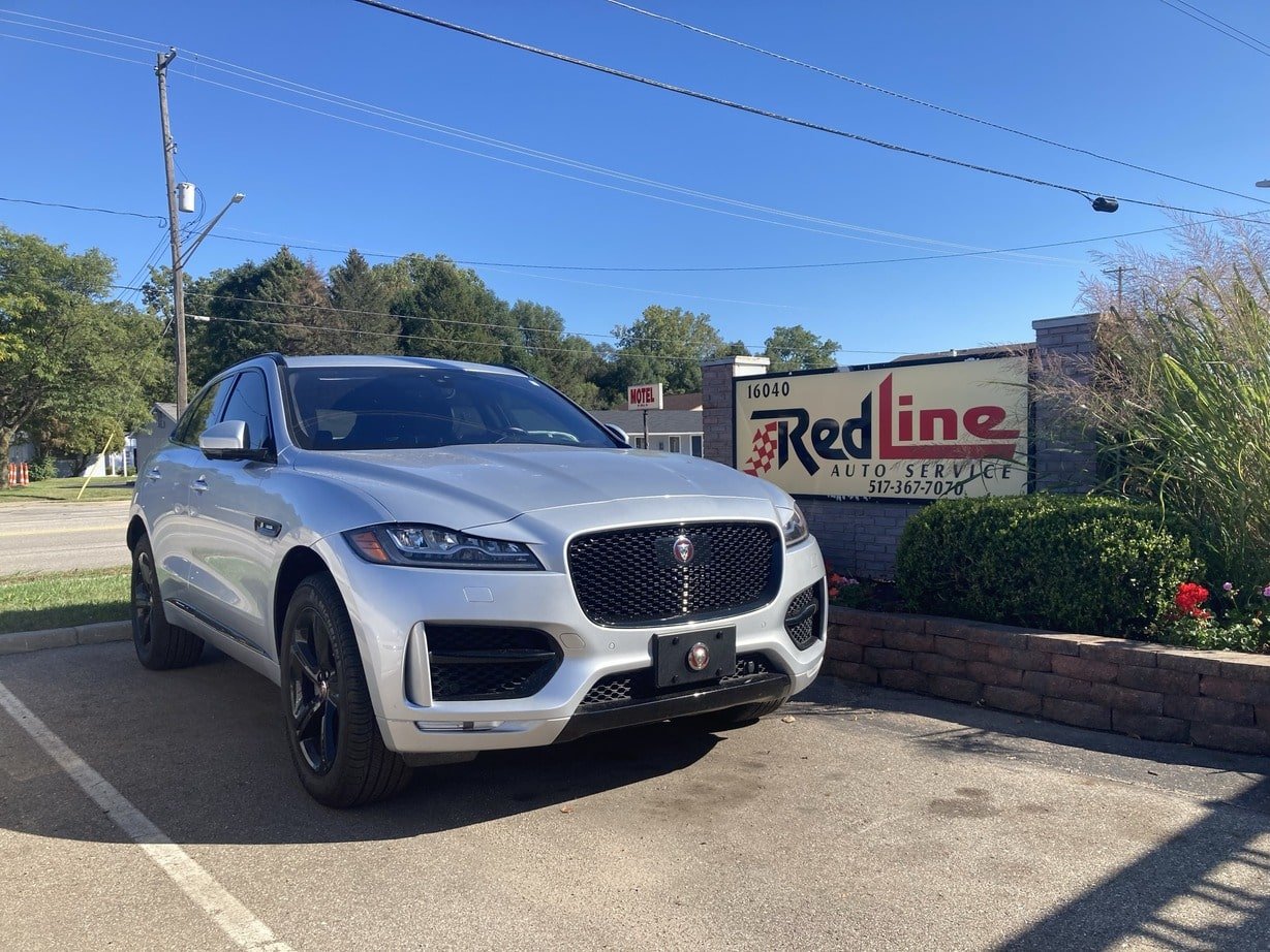 A silver luxury SUV parked outside a car service shop named Red Line Auto Service with a sign displaying the phone number 517-367-7070.