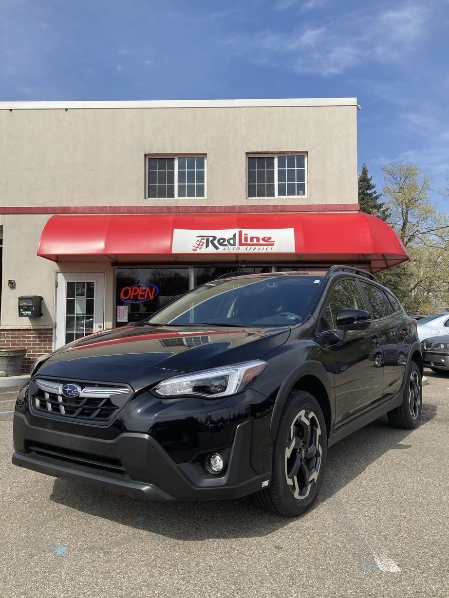 A black Subaru crossover parked in front of a red canopy with a sign that reads 'Red Line Auto Service' and a neon 'Open' sign in the window.