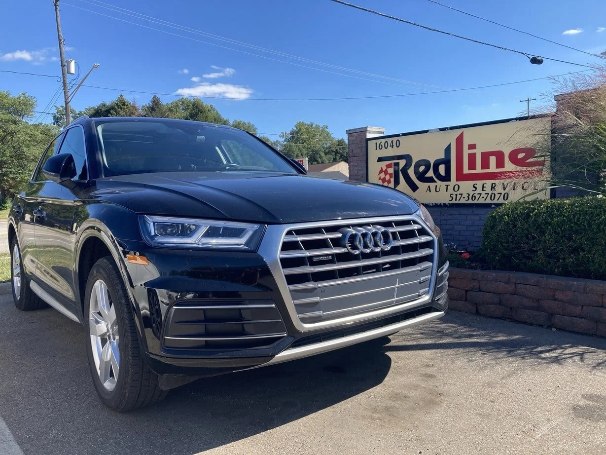 Black Audi SUV parked outside Red Line Auto Service with blue sky and greenery in the background.