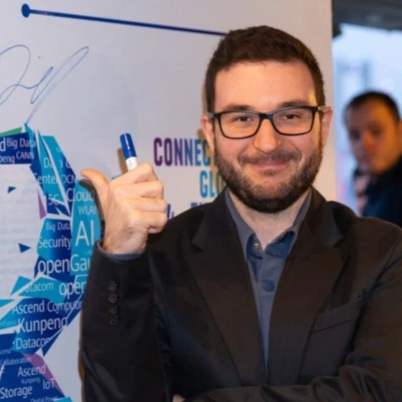 Man with glasses smiling and holding a marker in front of a whiteboard at a tech event.