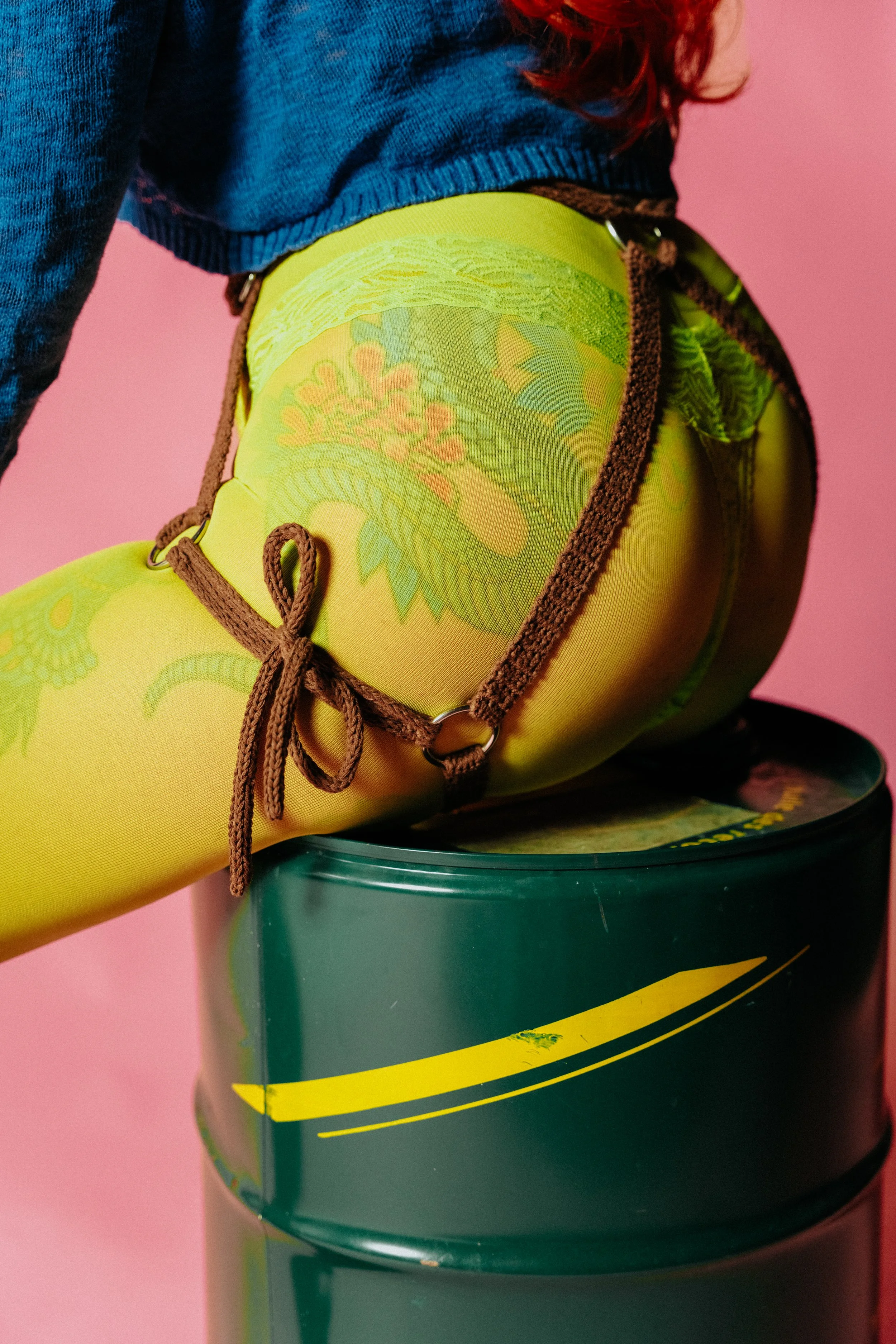 Close-up of a goalkeeper's hand wearing a yellow glove resting on a green sports barrel, with a pink background.