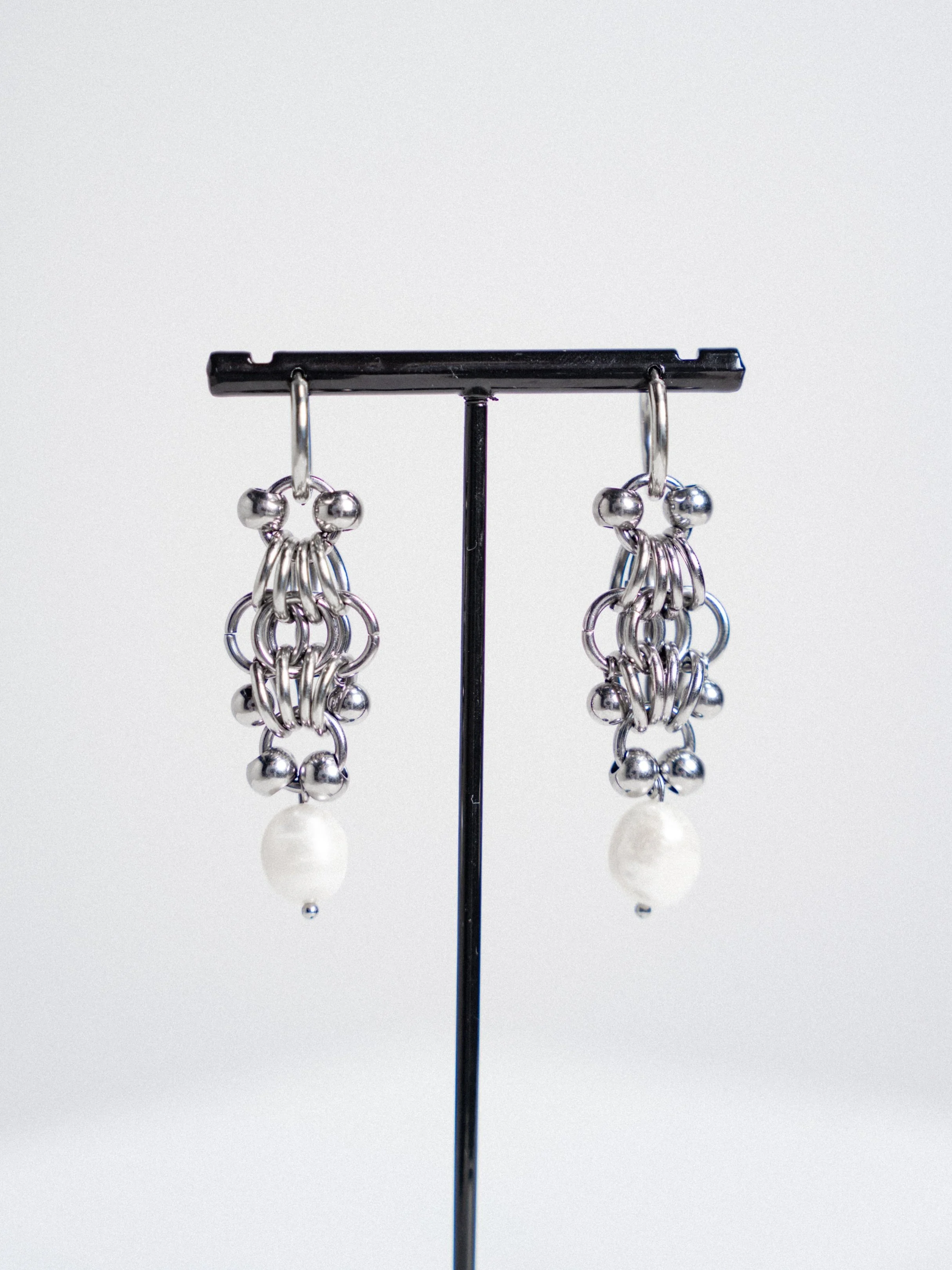 Silver chain-link earrings with pearl drops on display