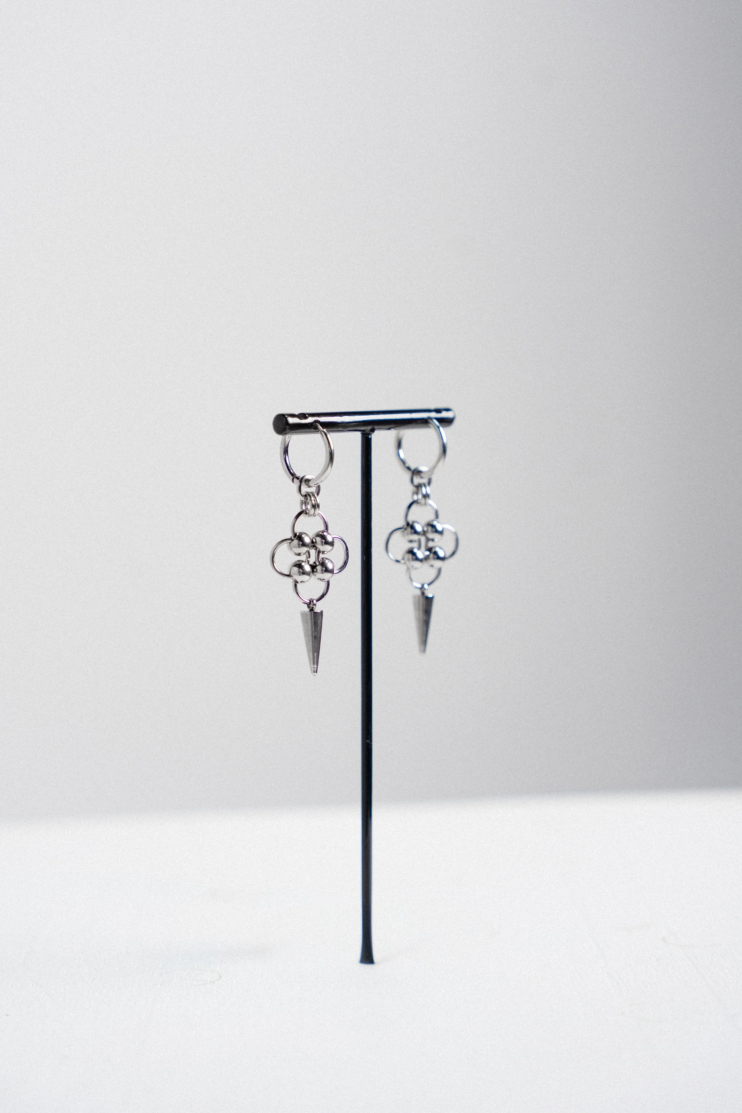 A pair of silver earrings with geometric and spike designs hanging from a black display stand against a plain background.